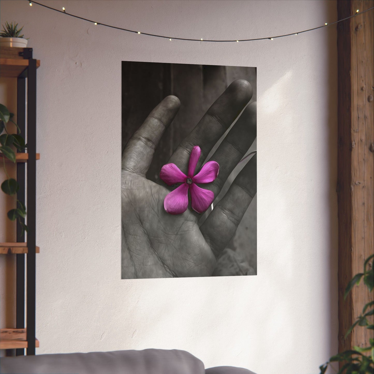 Poster of a hand holding a pink flower on a wall with decorative lights and plants.