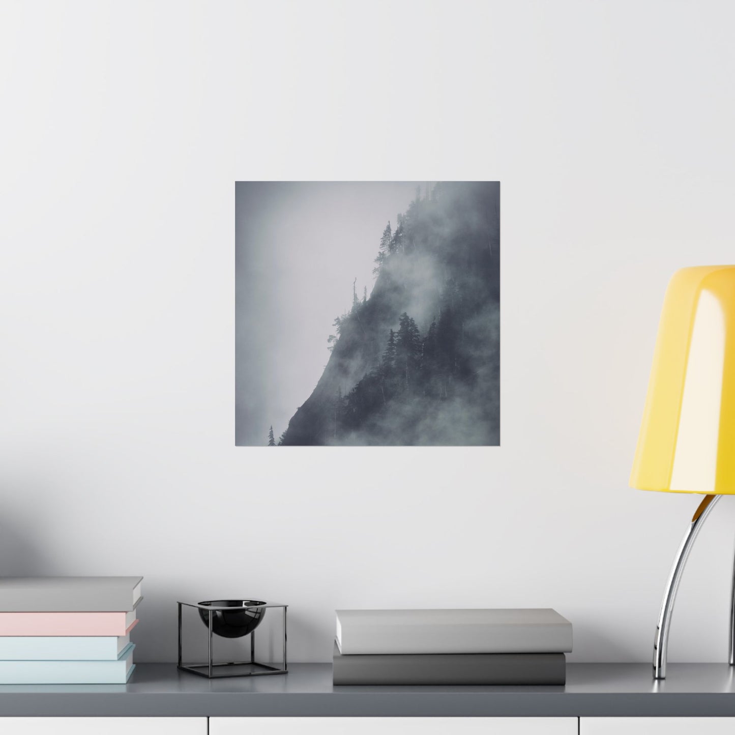 Framed artwork of a misty landscape on a wall above a shelf with books and decor items.