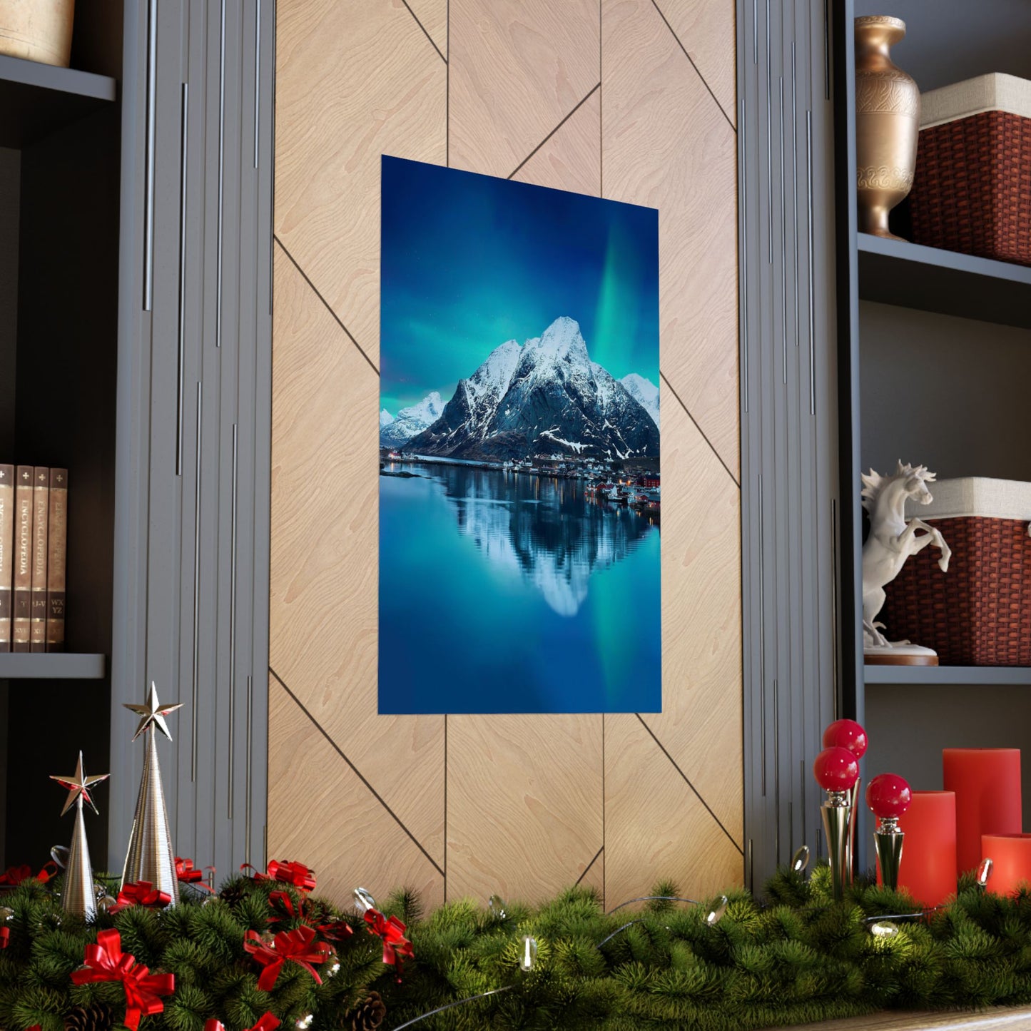 Framed mountain landscape with a lake and snowy peaks on a wall above holiday decorations.