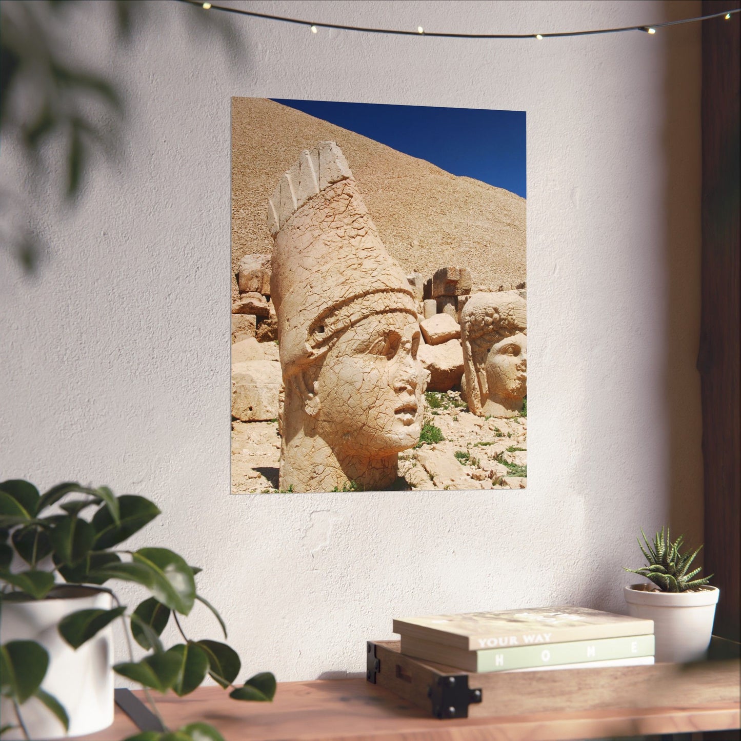Decorative wall art of stone heads on a white wall with plants and books below.