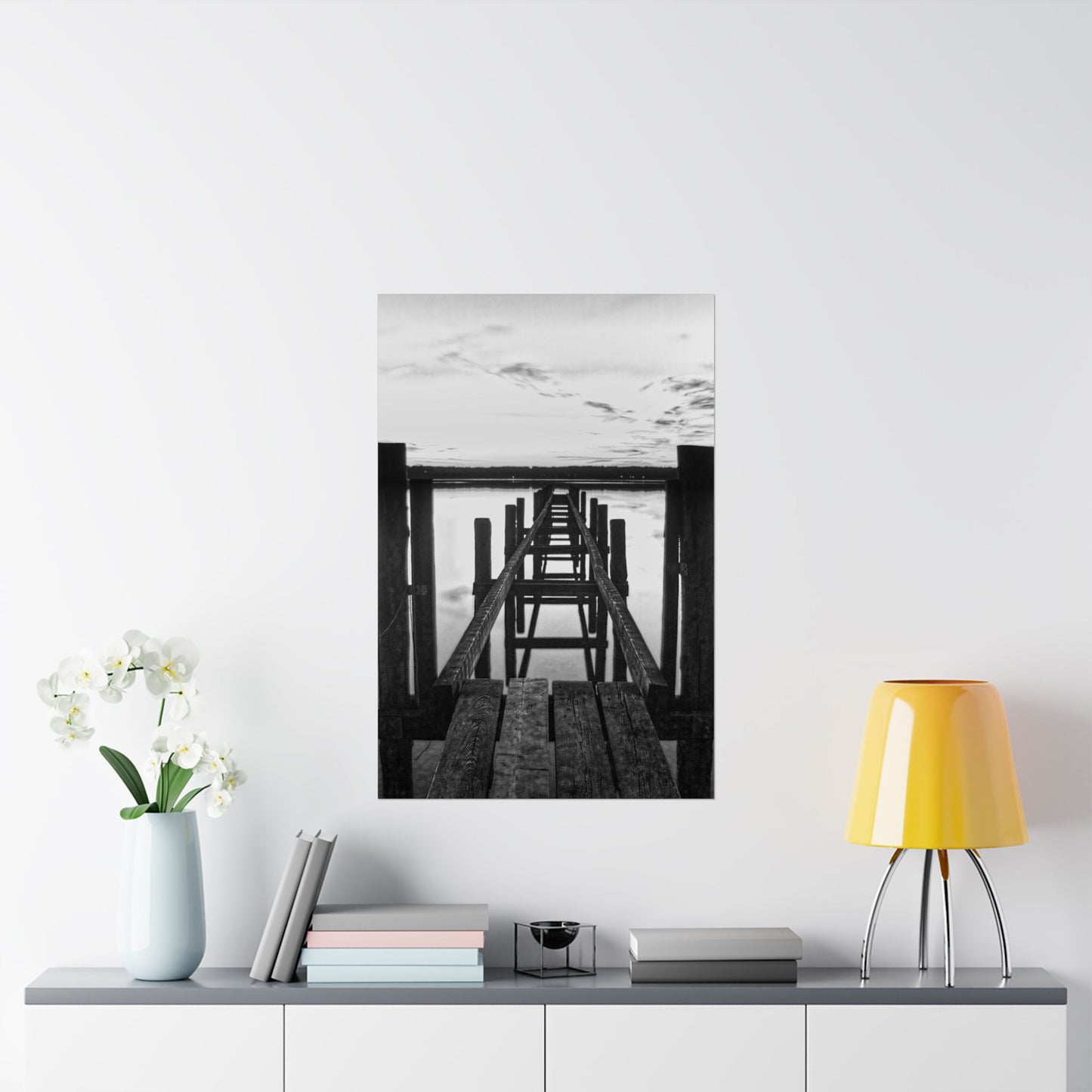 Framed black and white artwork of a dock on a wall above a shelf with decor items.