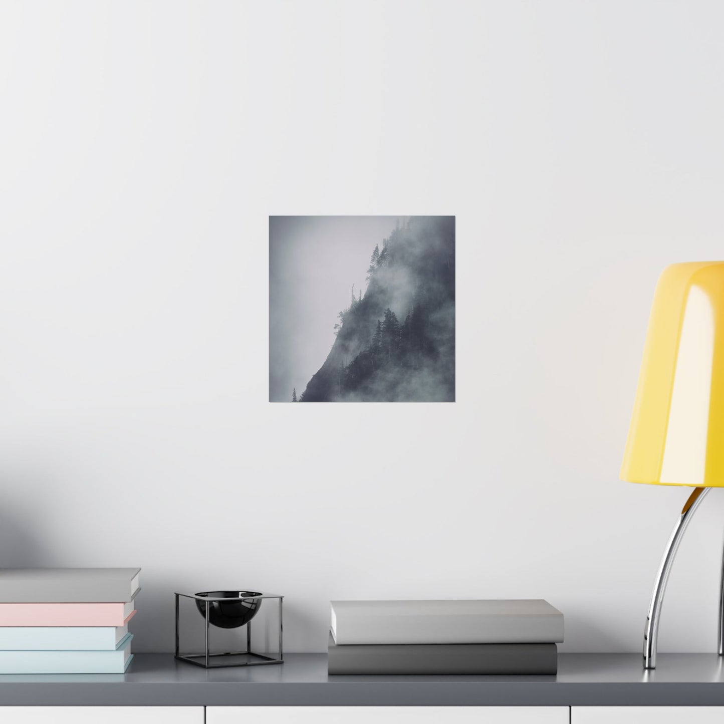 Art print of a mountain landscape on a wall above a desk with books and a lamp.