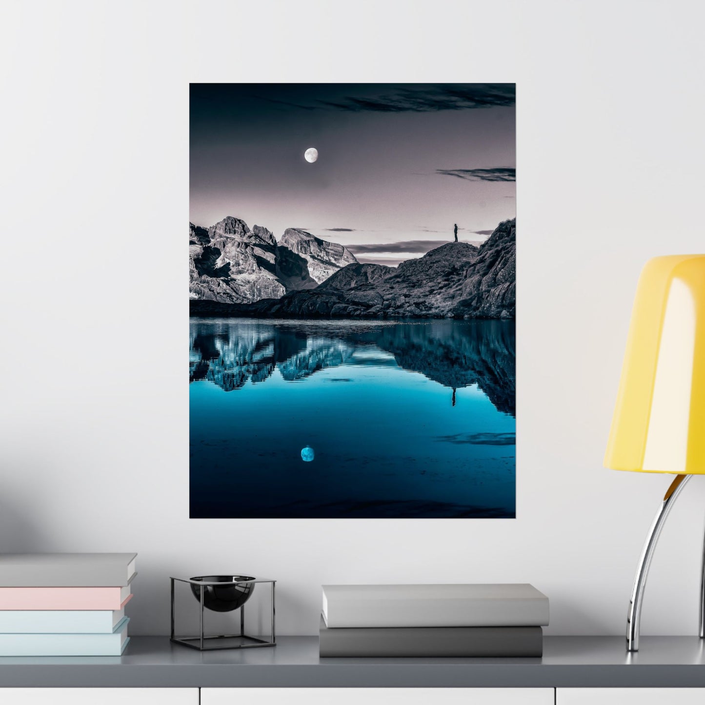 Framed mountain landscape with reflection in water on a wall above a shelf.