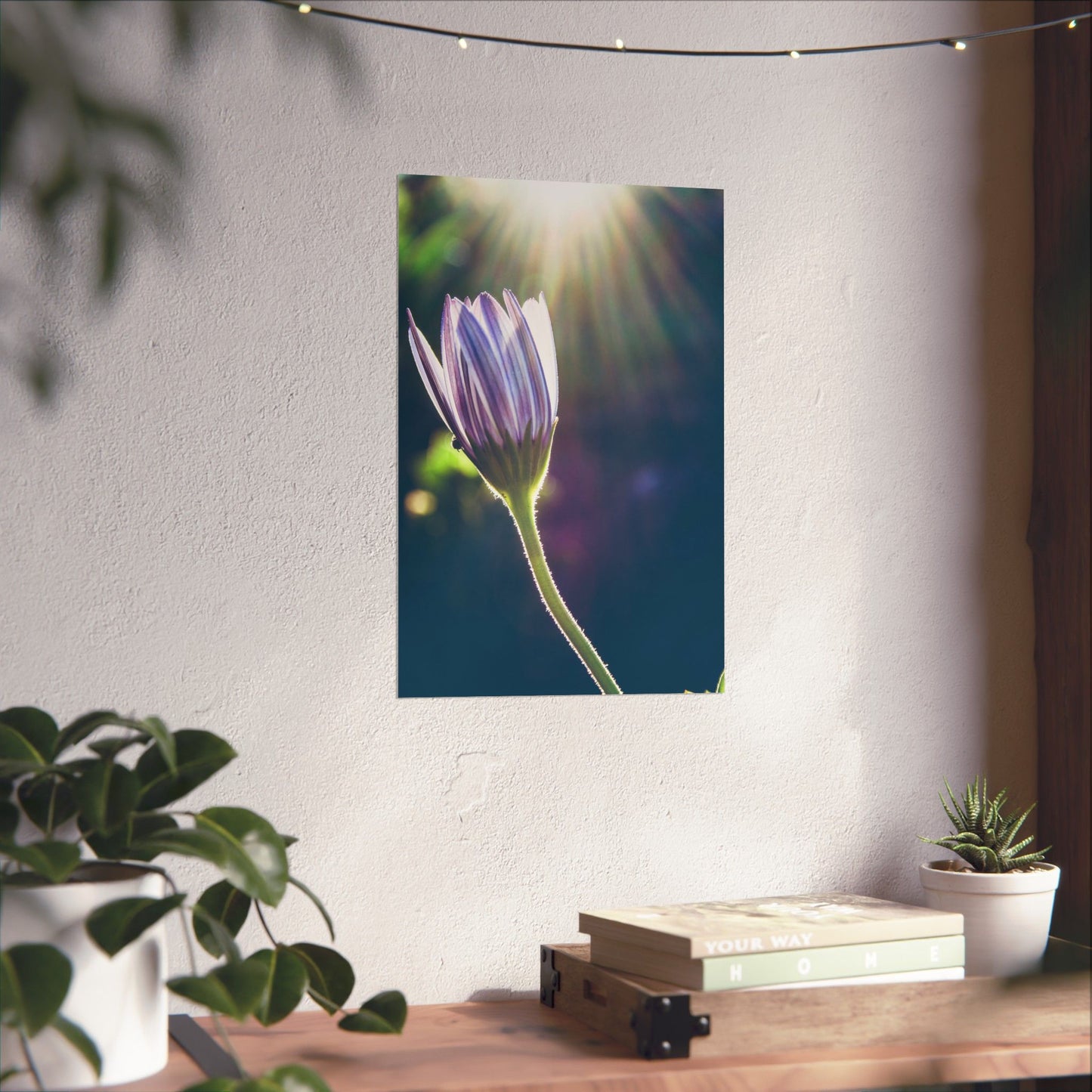 Flower poster on a wall with plants and books on a table below.