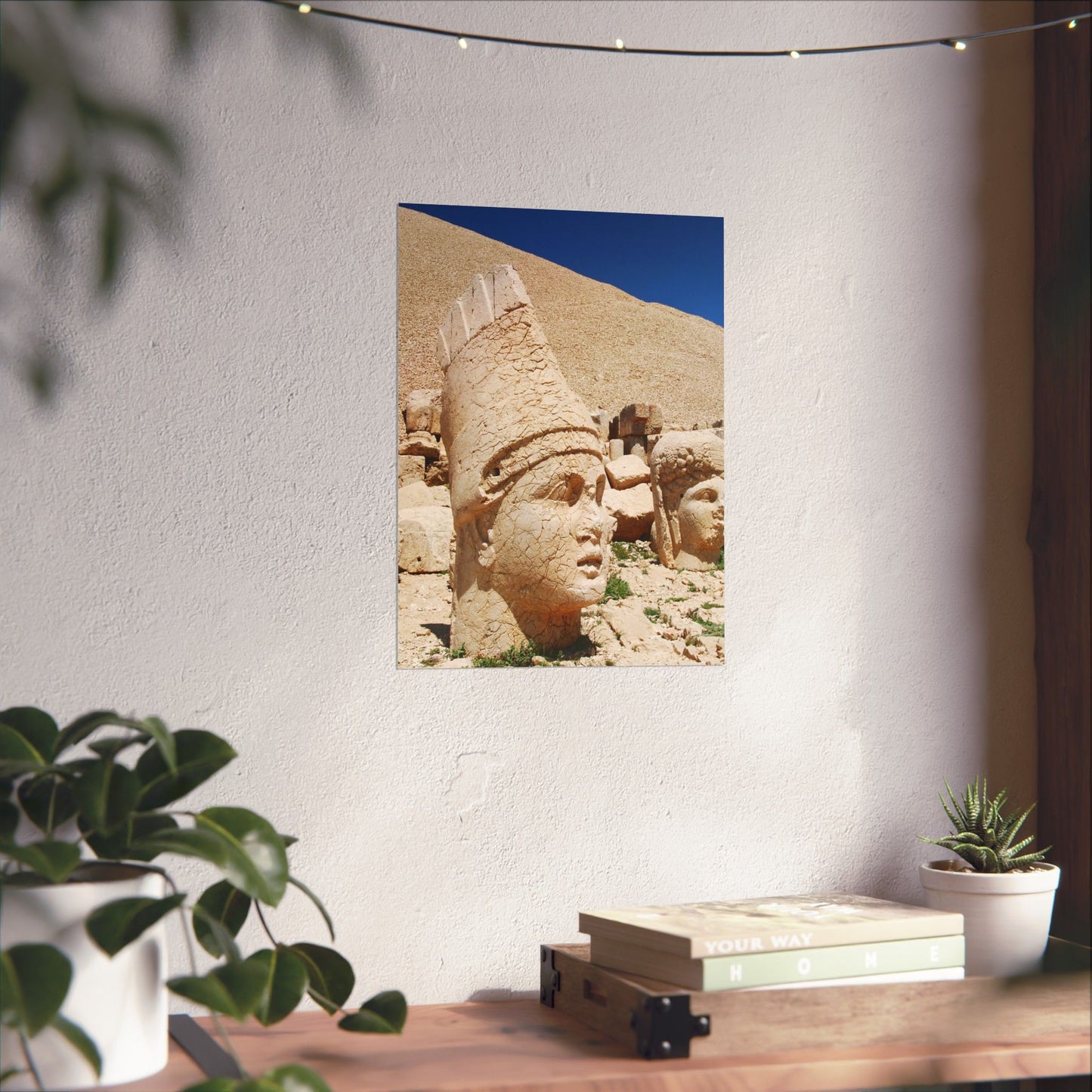 Framed picture of ancient stone faces on a wall above a desk with plants.