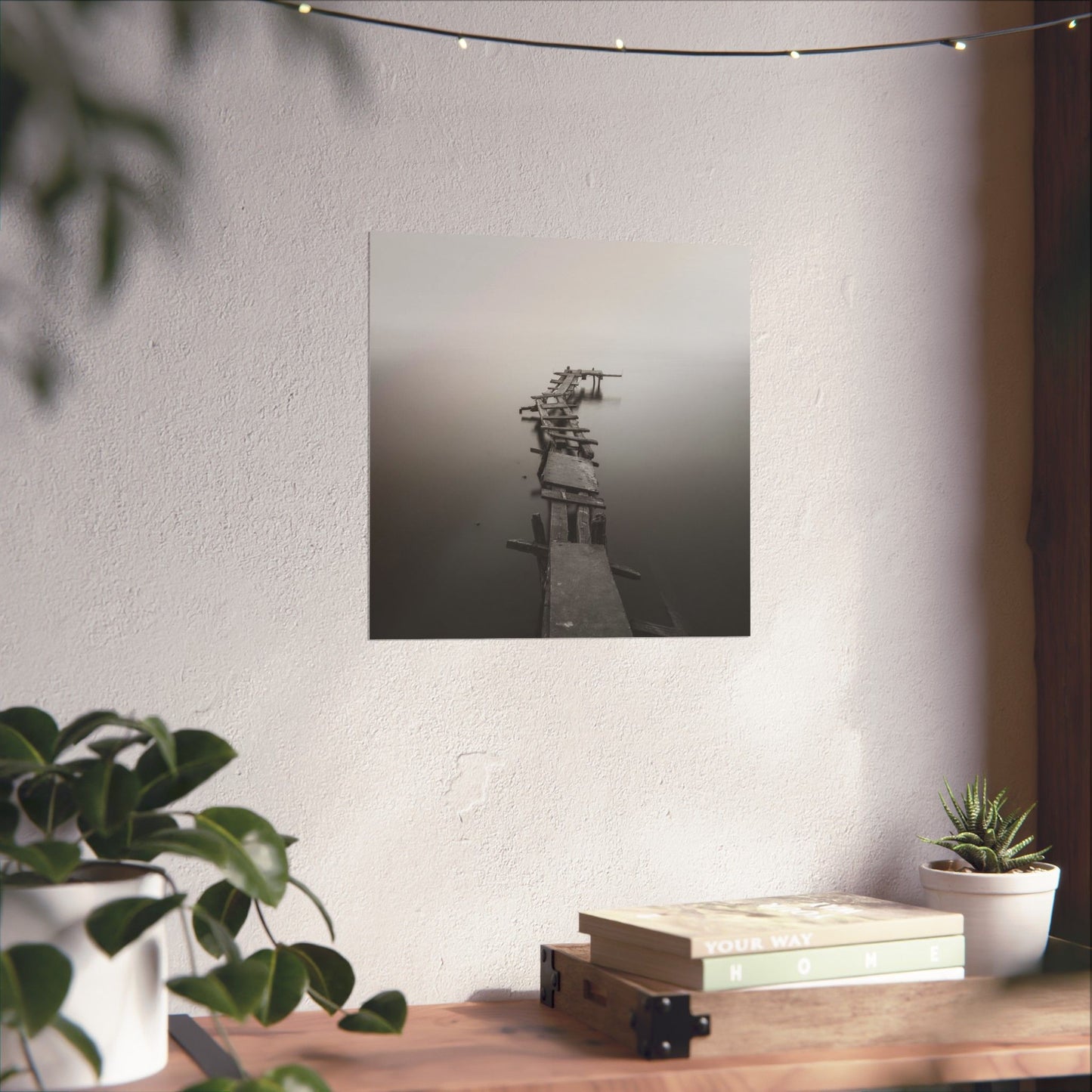Framed artwork of a dock on a white wall above a wooden table with plants.