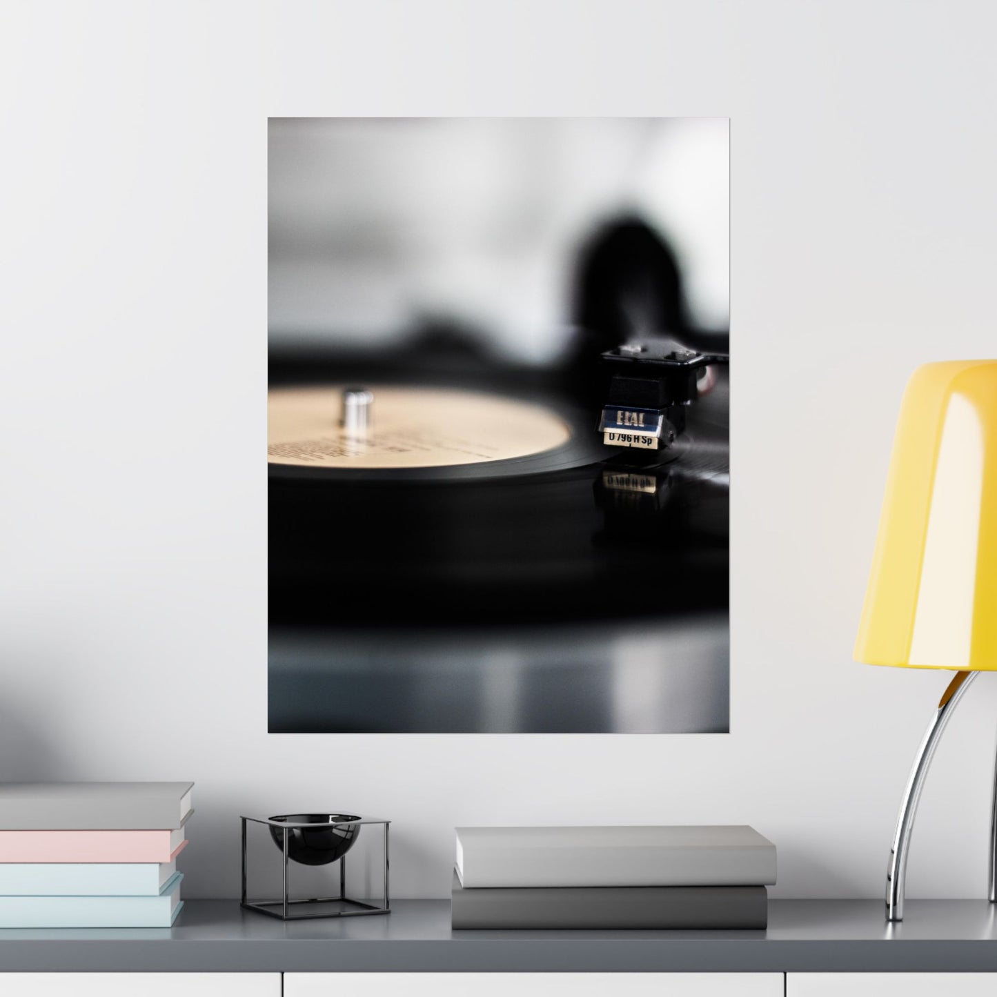 Modern interior with a shelf featuring books, a small bowl, and a yellow lamp against a white wall with a framed abstract art piece.