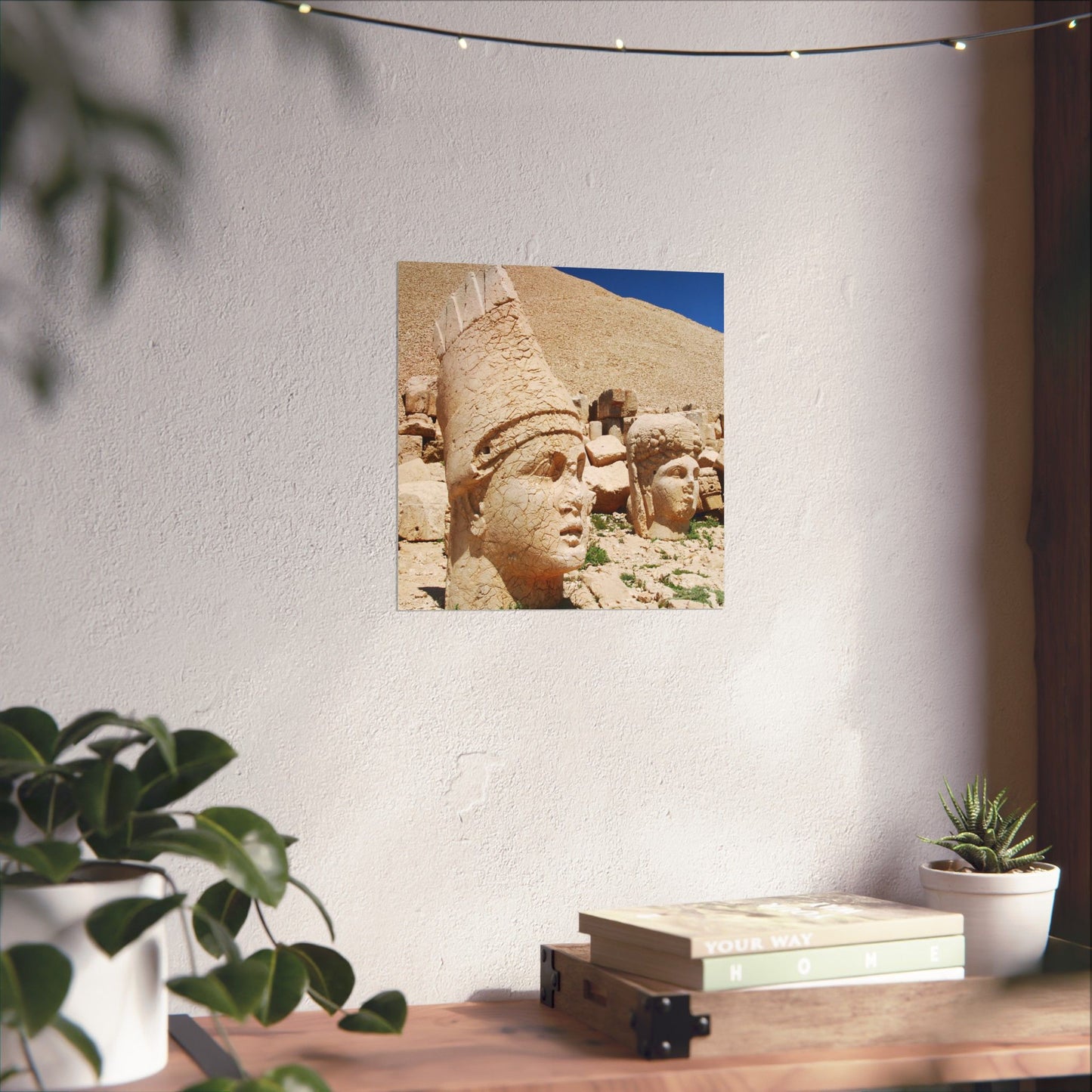 Decorative wall art of ancient stone carvings on a white wall with plants and books below.