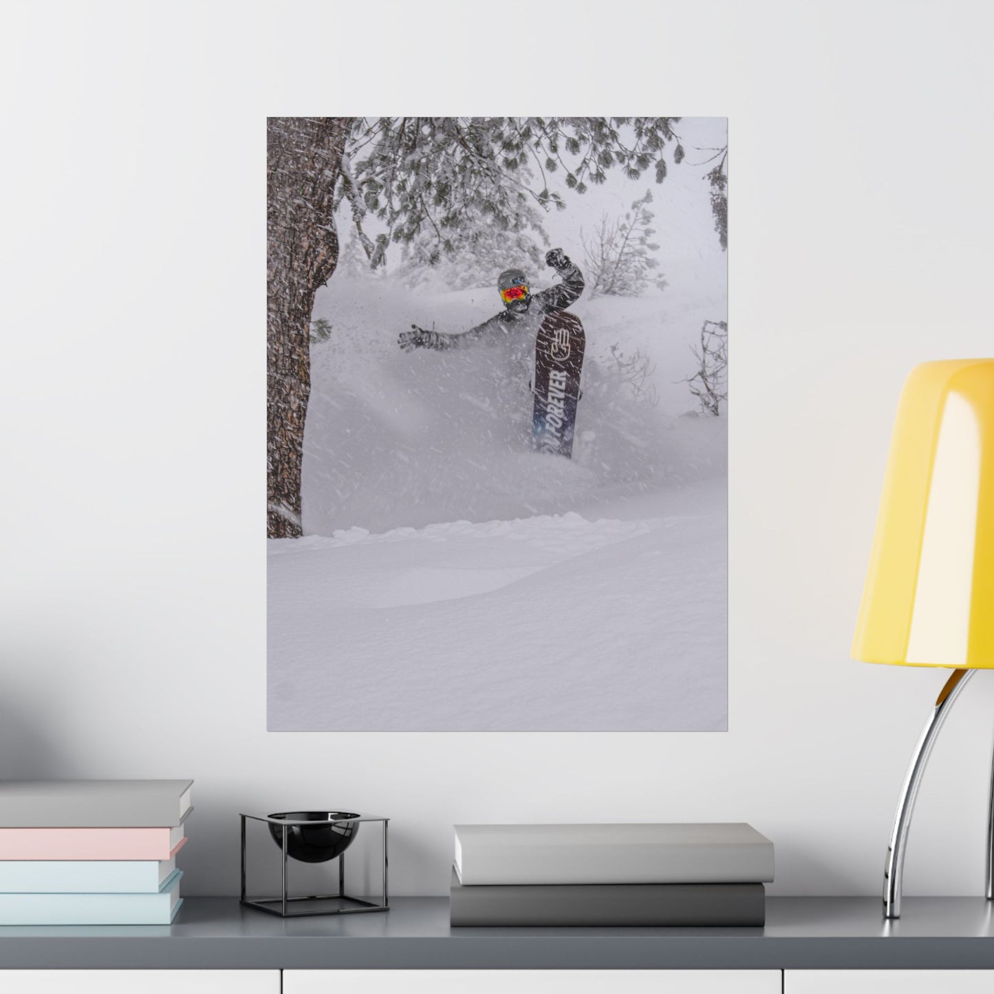 Poster of a person snowboarding on a wall above a desk with books and a lamp.