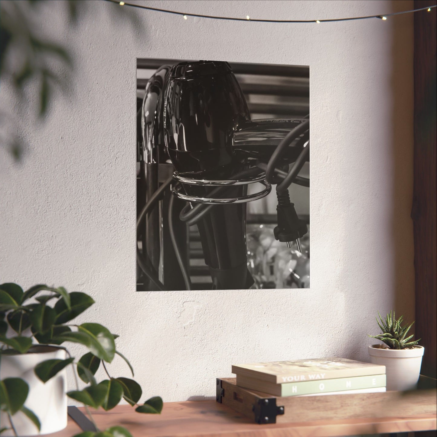Black and white photo of a lamp on a wall with plants and books on a table below.