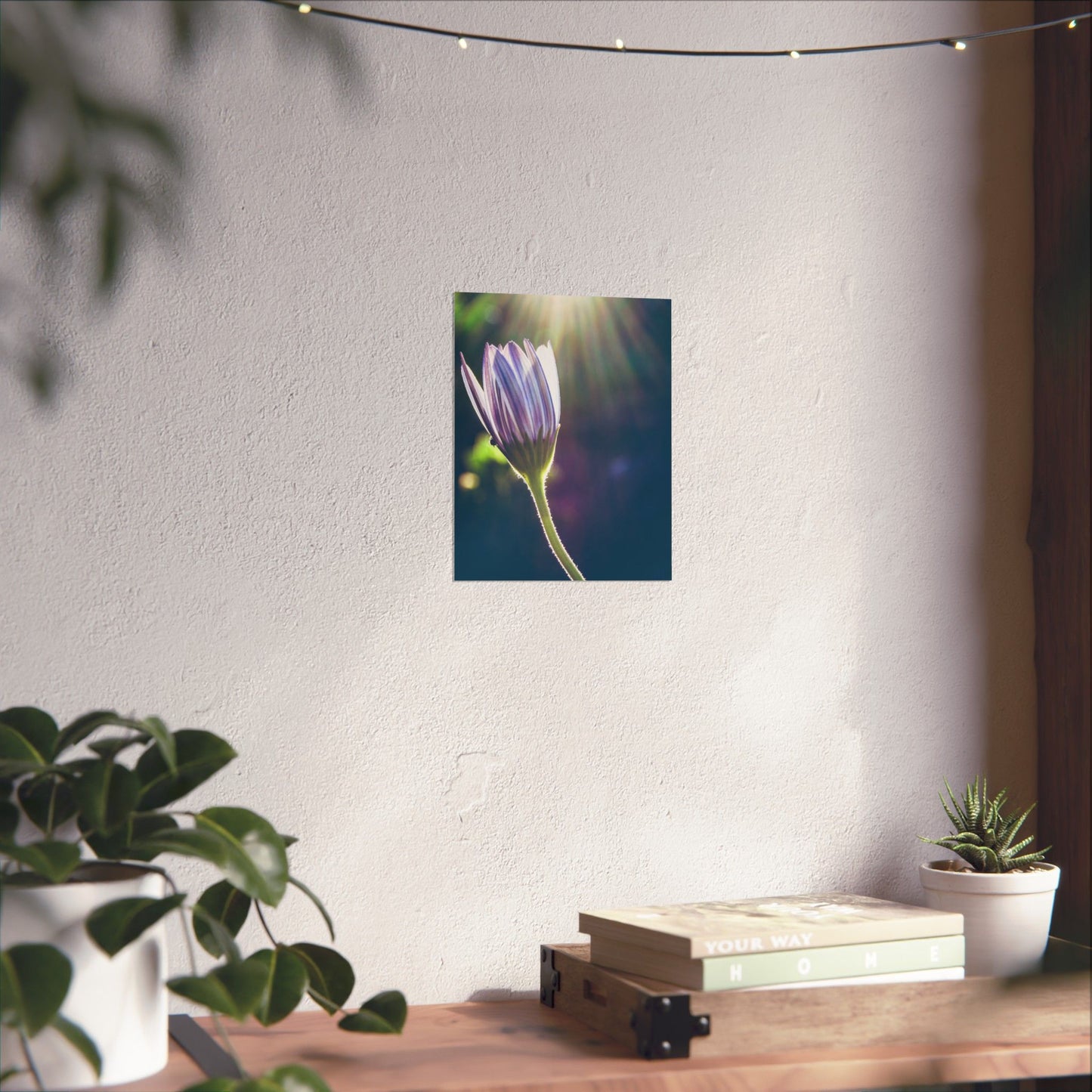 Wall art of a purple flower on a white wall with plants and books below.