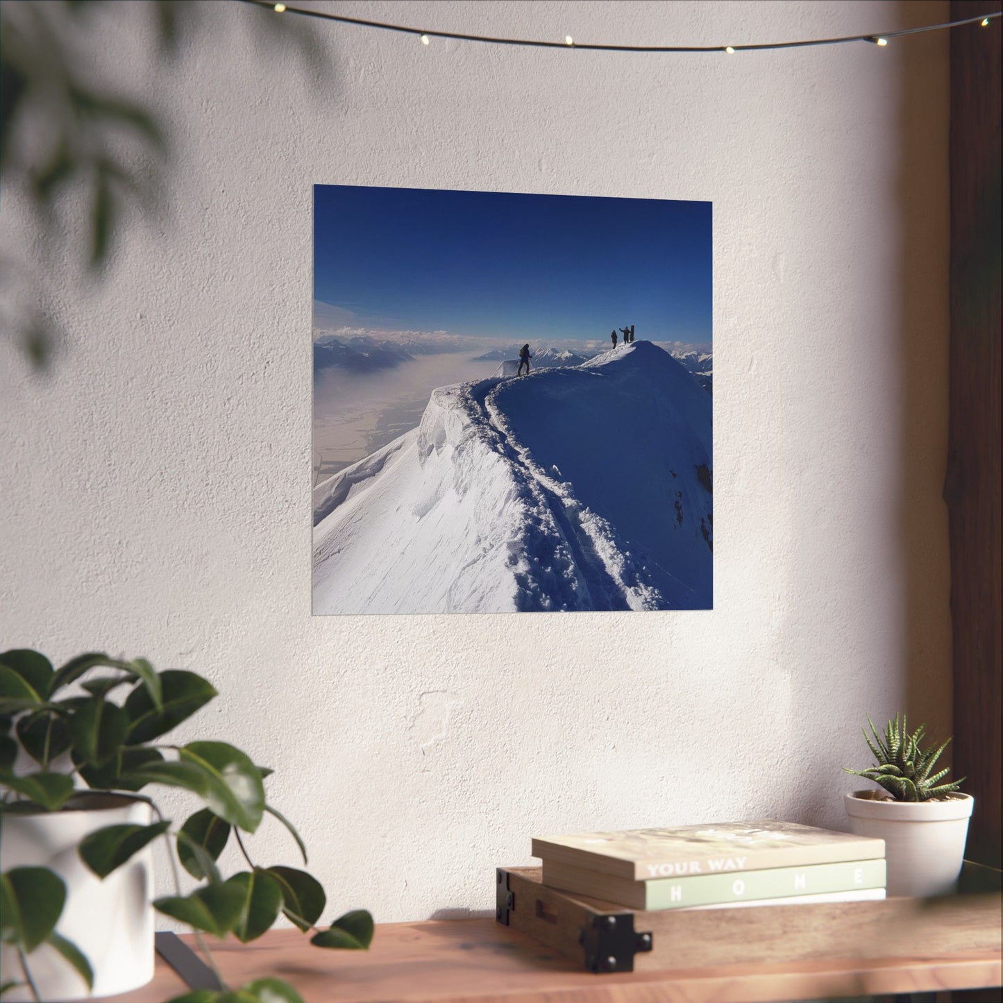 Framed photograph of a snowy mountain landscape on a wall above a desk with plants.