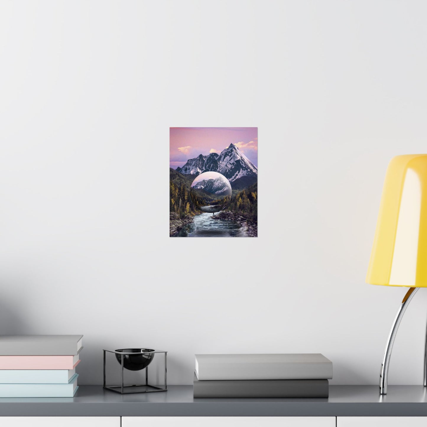 Framed artwork of a mountain landscape with a purple sky on a white wall above a desk.