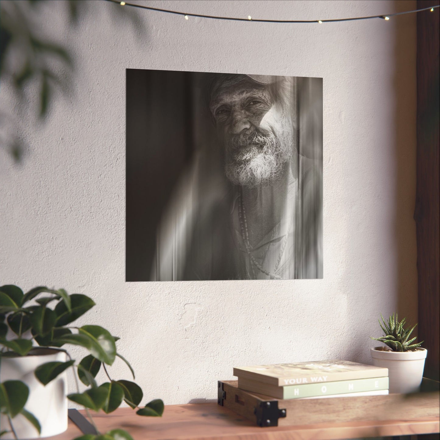 Black and white portrait of a man with a beard on a wall above a wooden desk with plants and books.