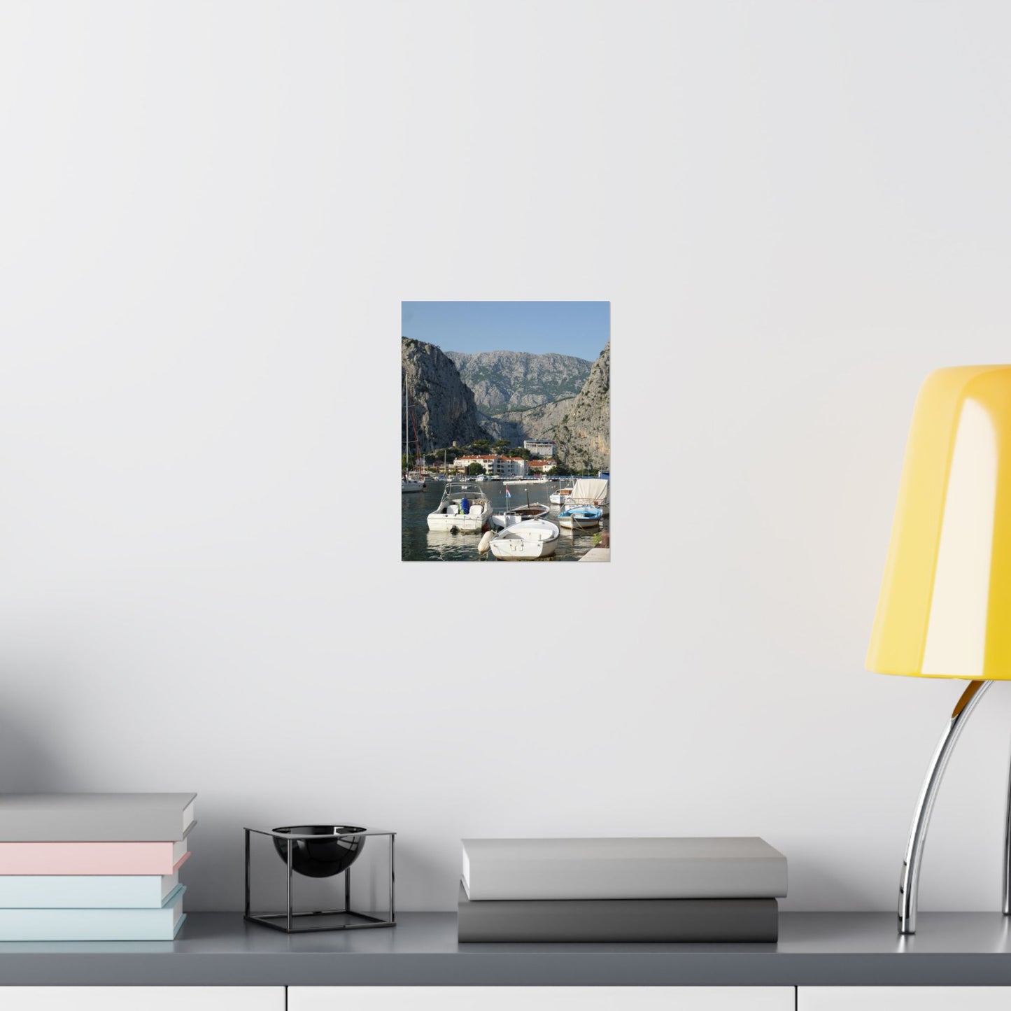 Framed photograph of a coastal scene on a wall above a desk with books and a lamp.