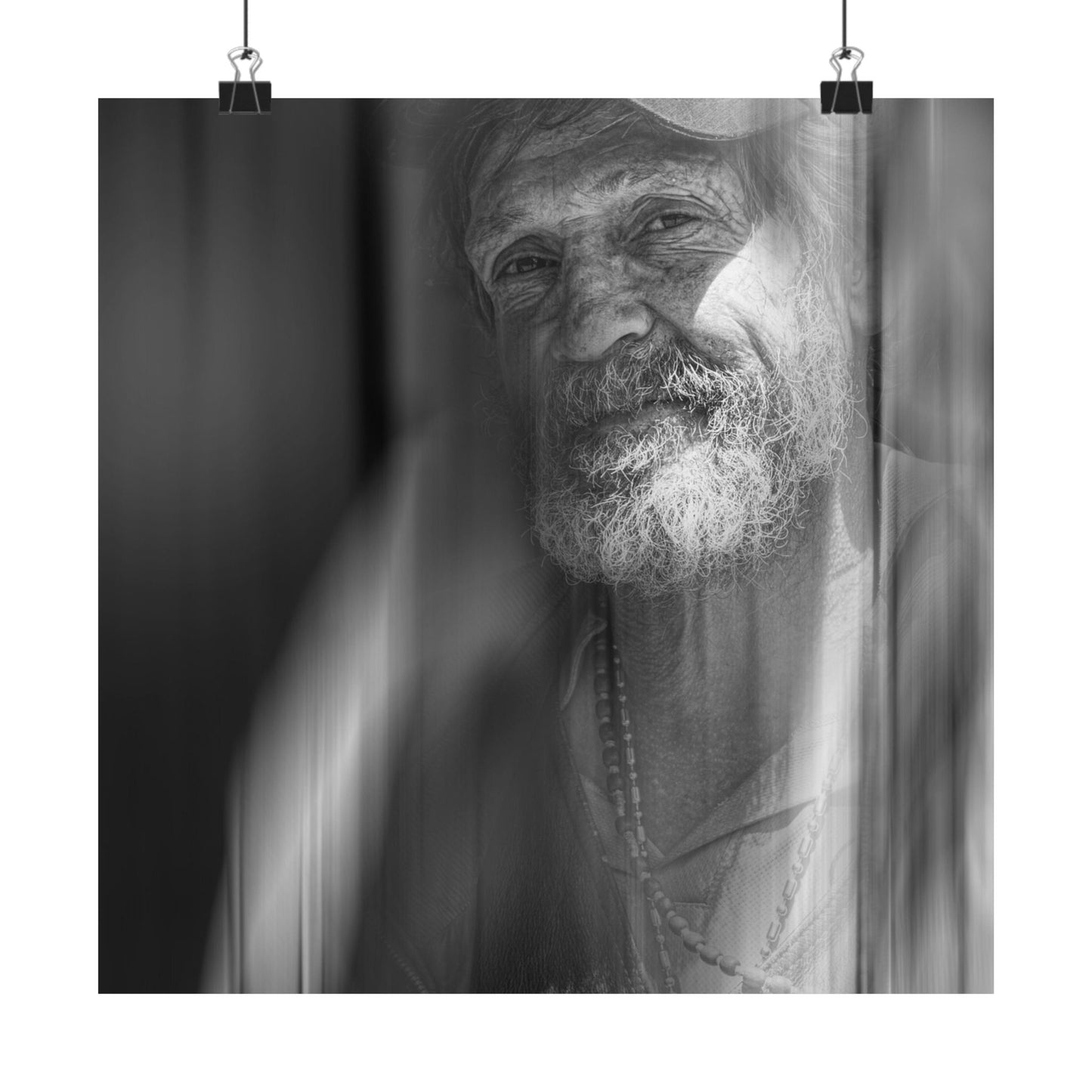Black and white portrait of a man with a beard and necklace, framed by curtains.
