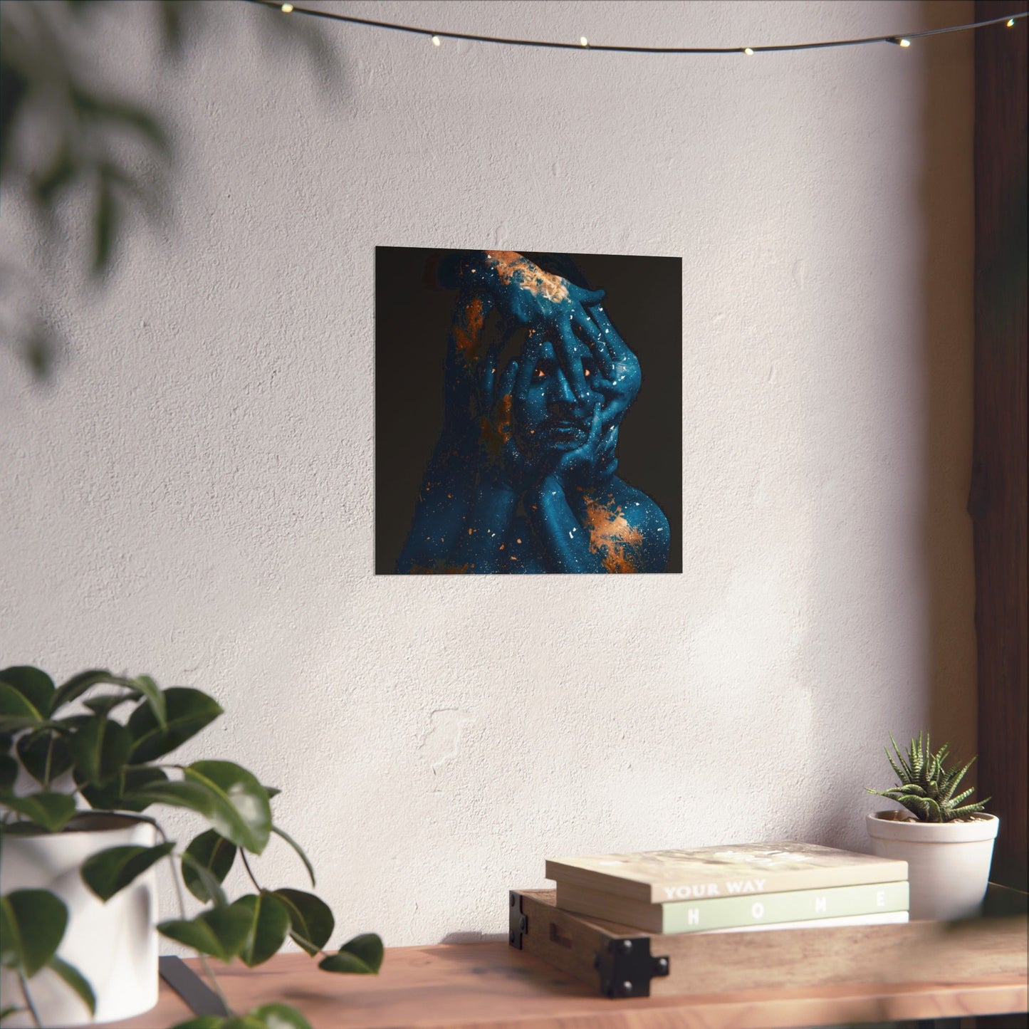Abstract painting of a face on a wall above a wooden table with plants and books.