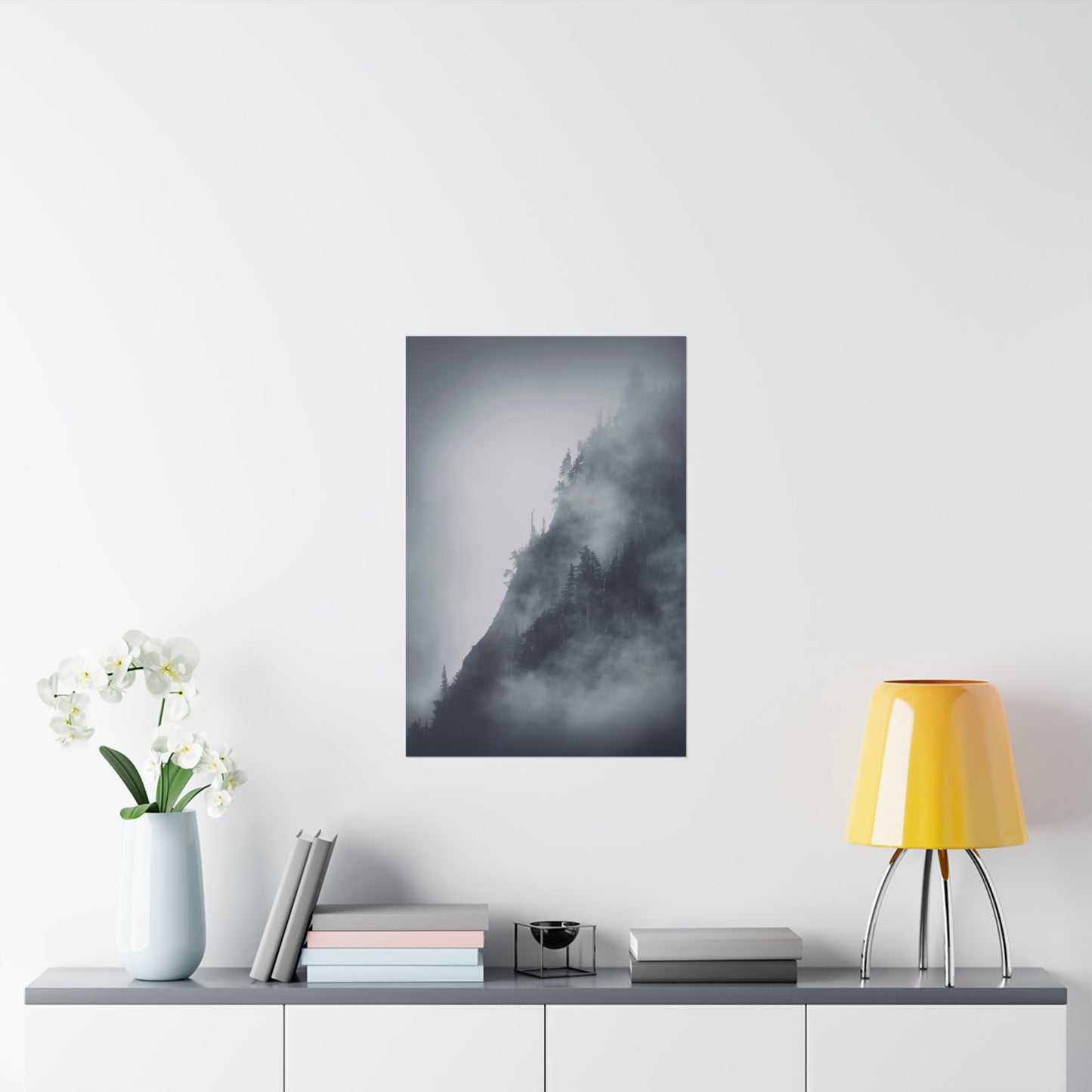 Framed black and white mountain landscape art on a wall above a shelf with decor items.