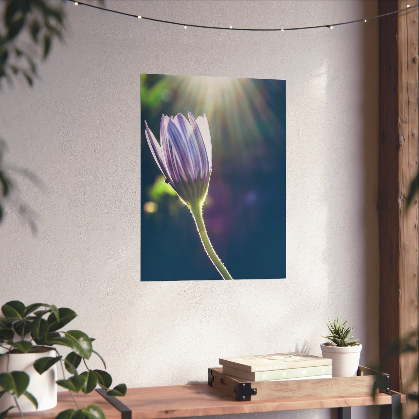 Flower painting on a wall above a wooden table with books and plants.