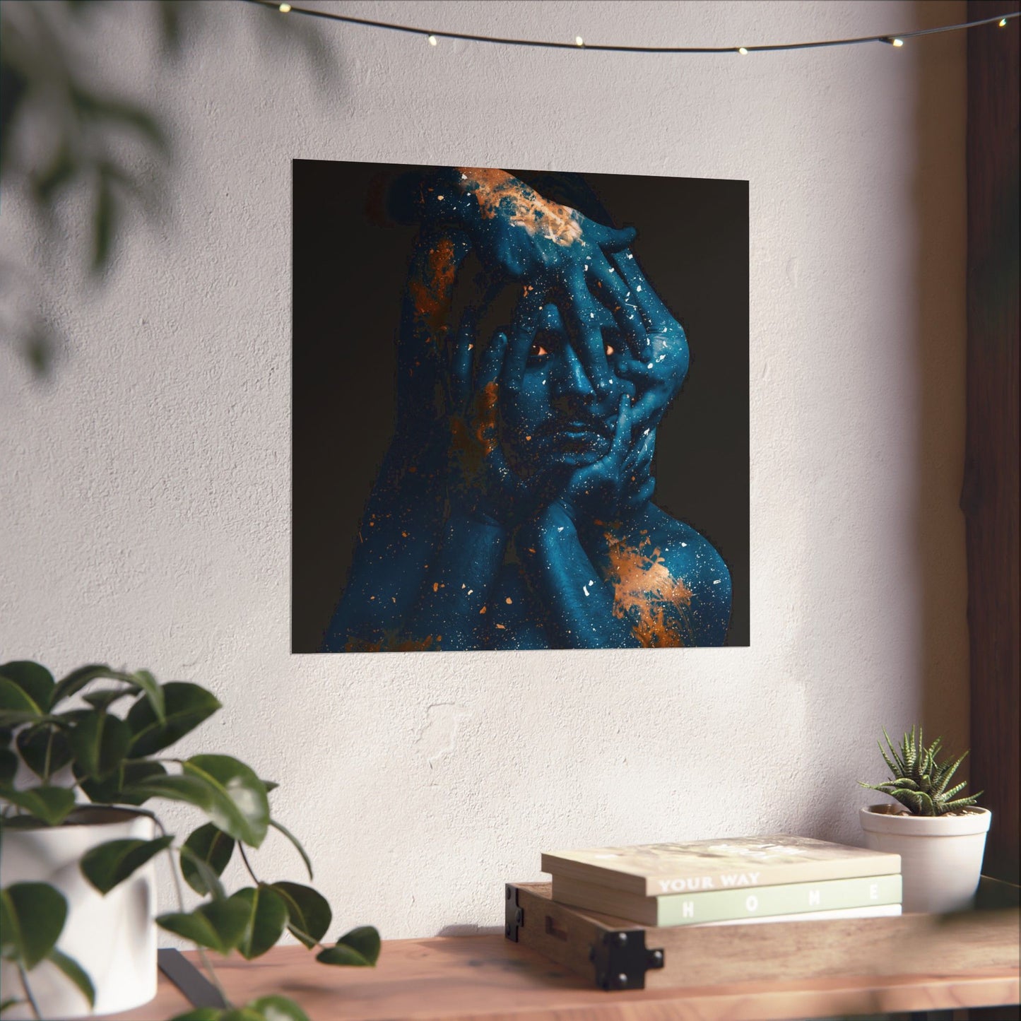 Abstract art piece of a blue and orange figure on a white wall above a wooden desk with plants.