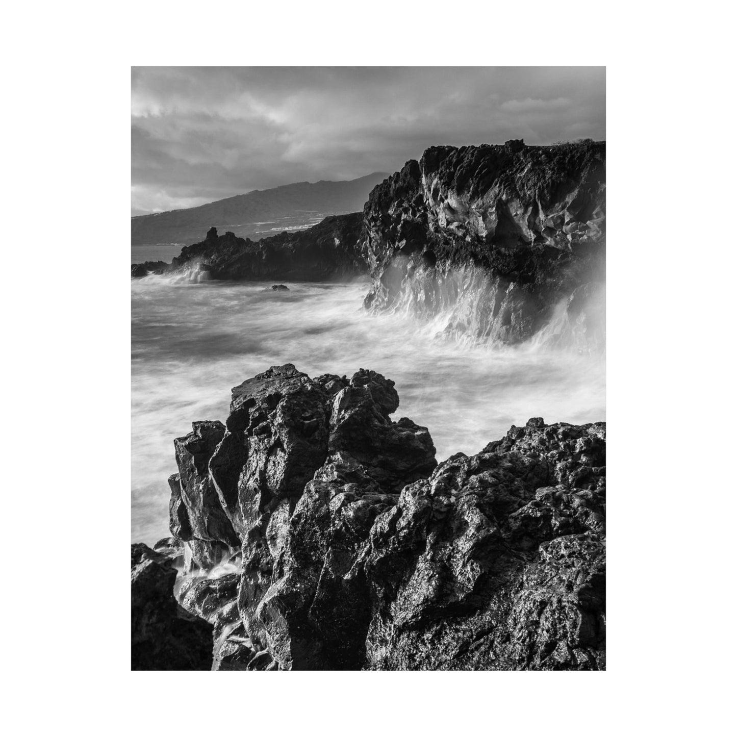 Black and white photograph of a rocky coastline with waves crashing against the rocks.