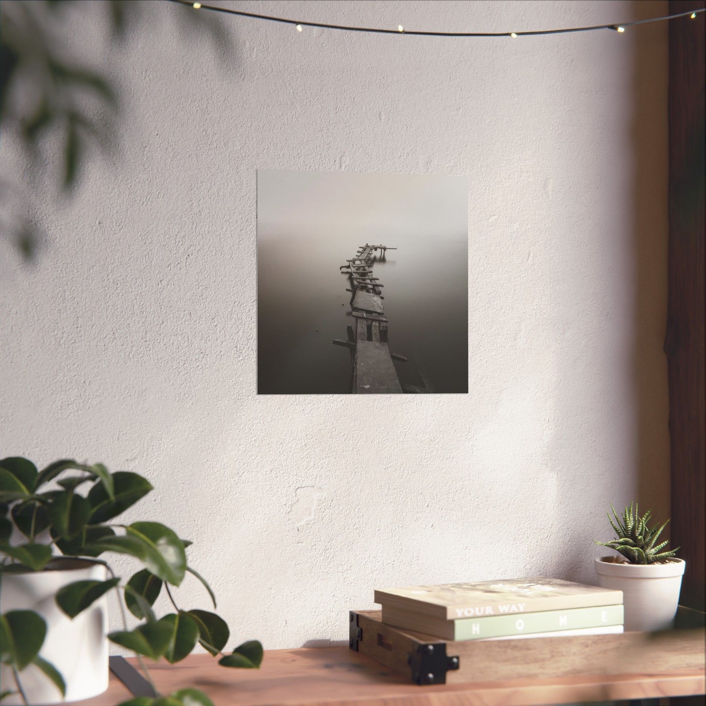 Framed black and white photograph on a wall above a wooden desk with plants and books.