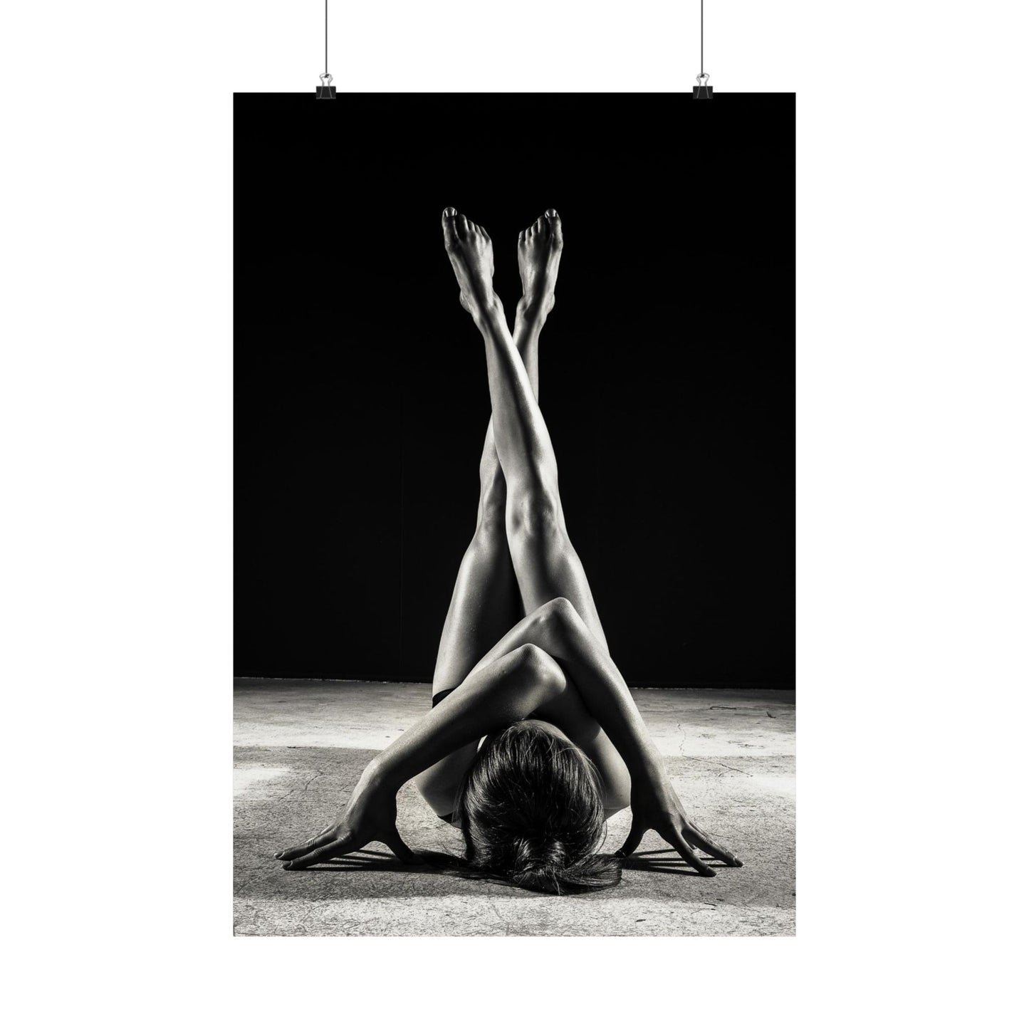 Black and white photograph of a person in a yoga pose with legs extended upwards against a dark background.