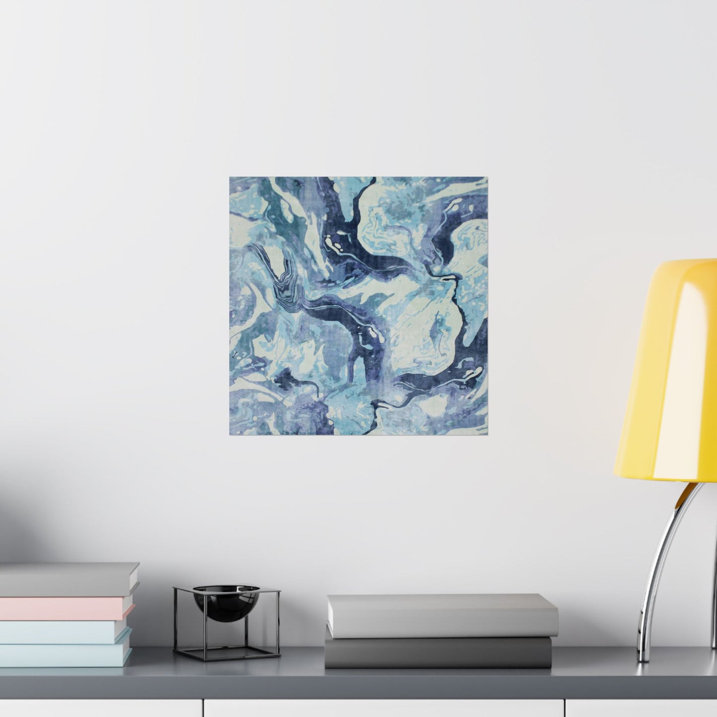 Abstract blue and green painting on a white wall above a shelf with books and a lamp.