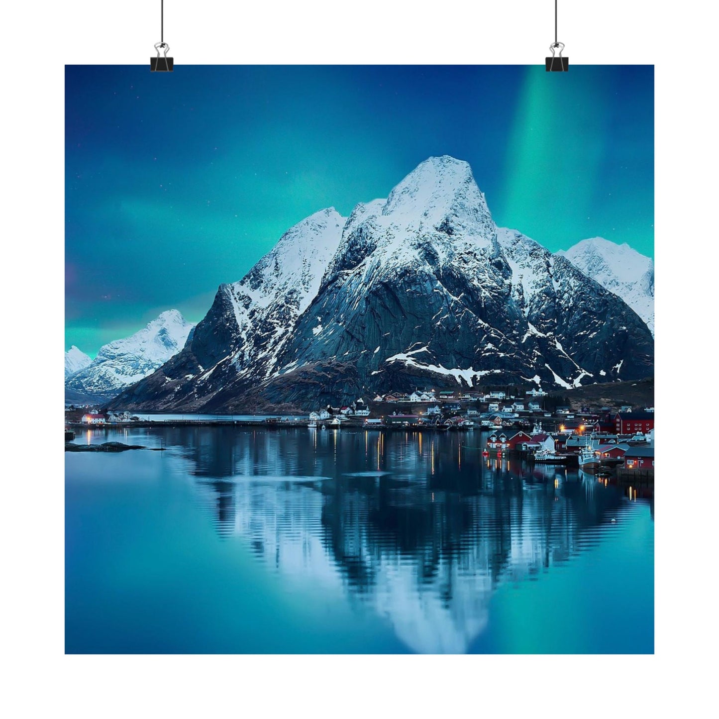Snow-covered mountain reflecting in a lake with a town below under a dark blue sky.