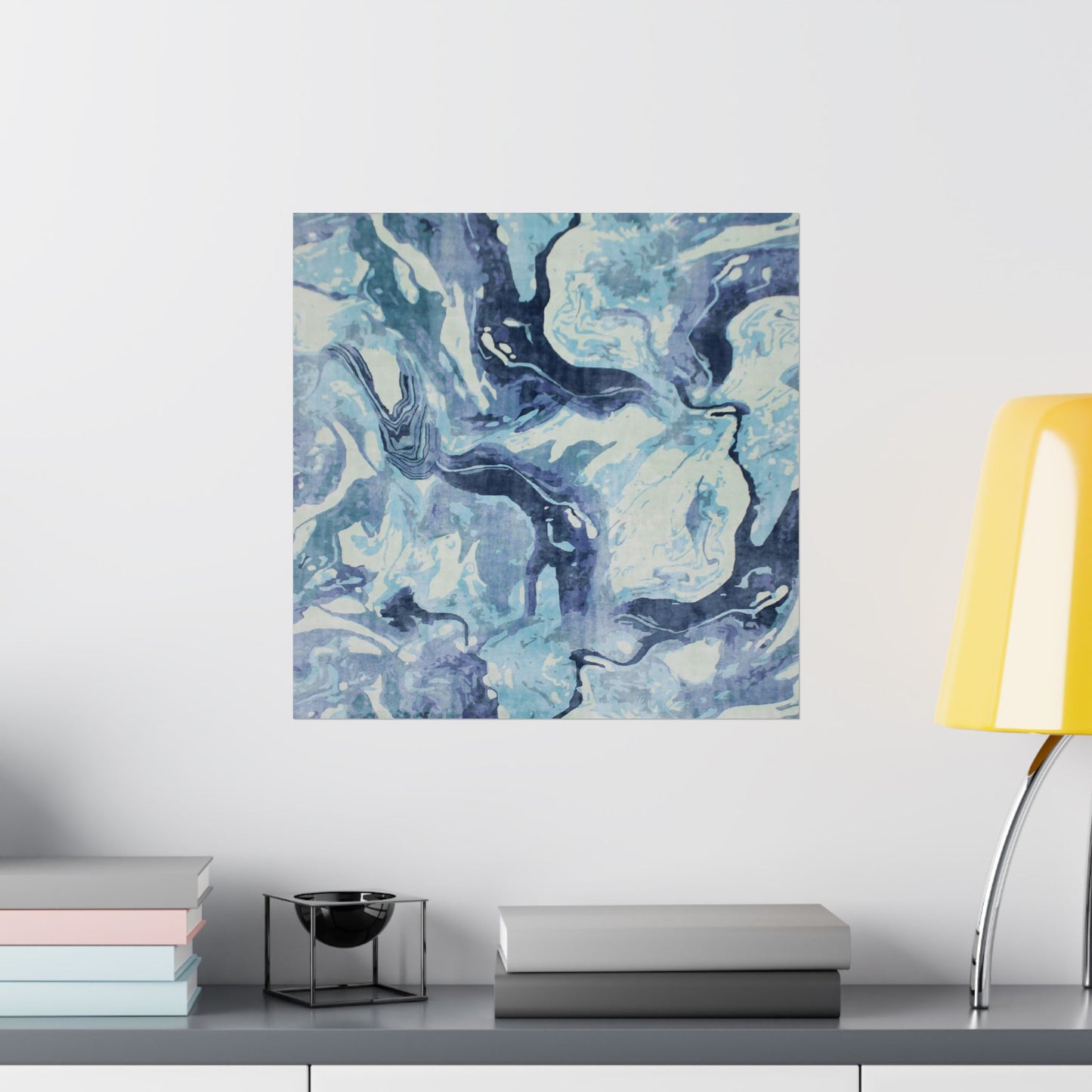 Abstract blue and white painting on a wall above a shelf with books and a lamp.
