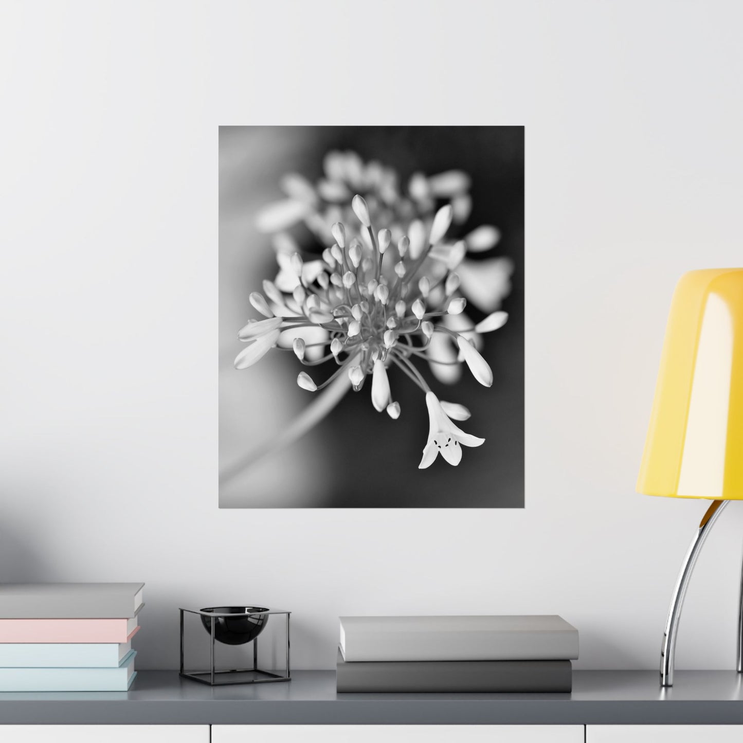 Floral artwork on a wall above a shelf with books and a lamp.