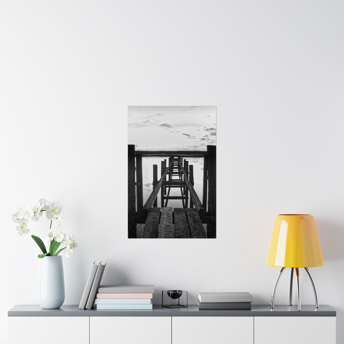 Framed black and white artwork on a wall above a shelf with decor items.
