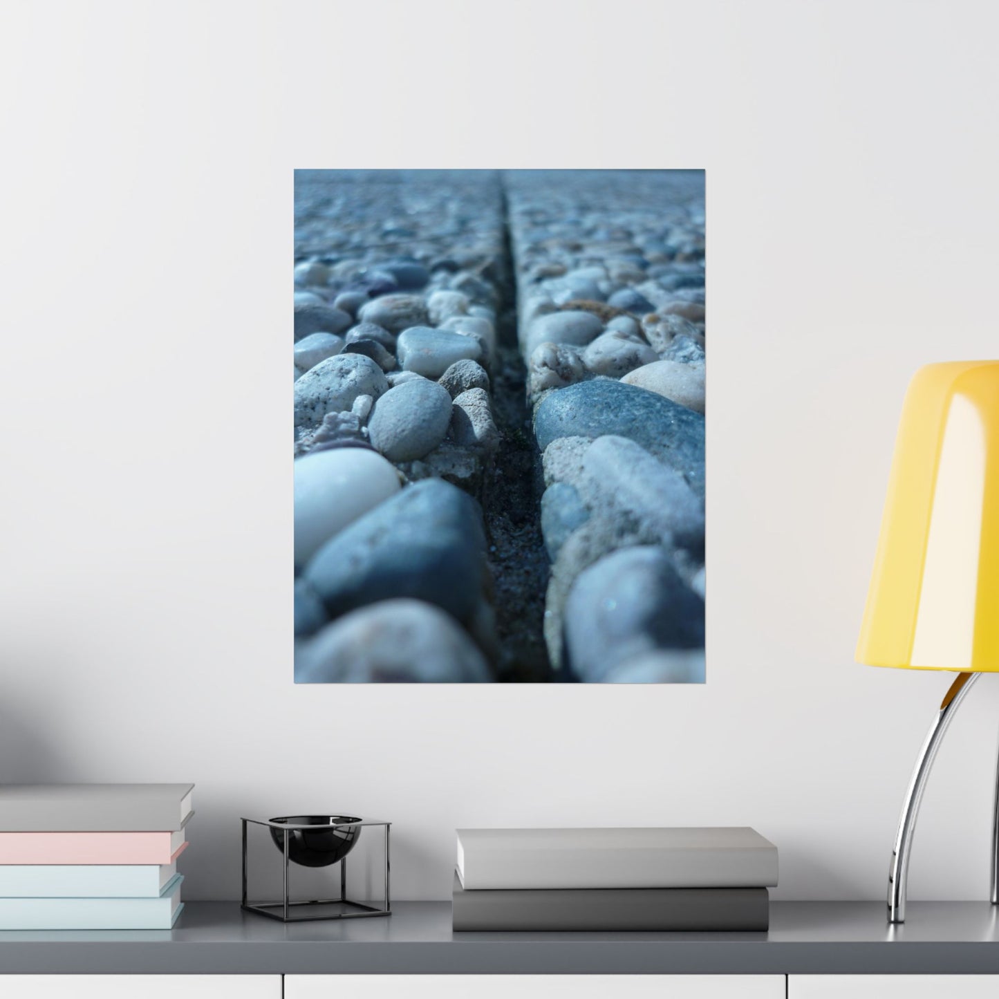 Framed photograph of textured blue surface on a wall above a shelf with books and decor items.