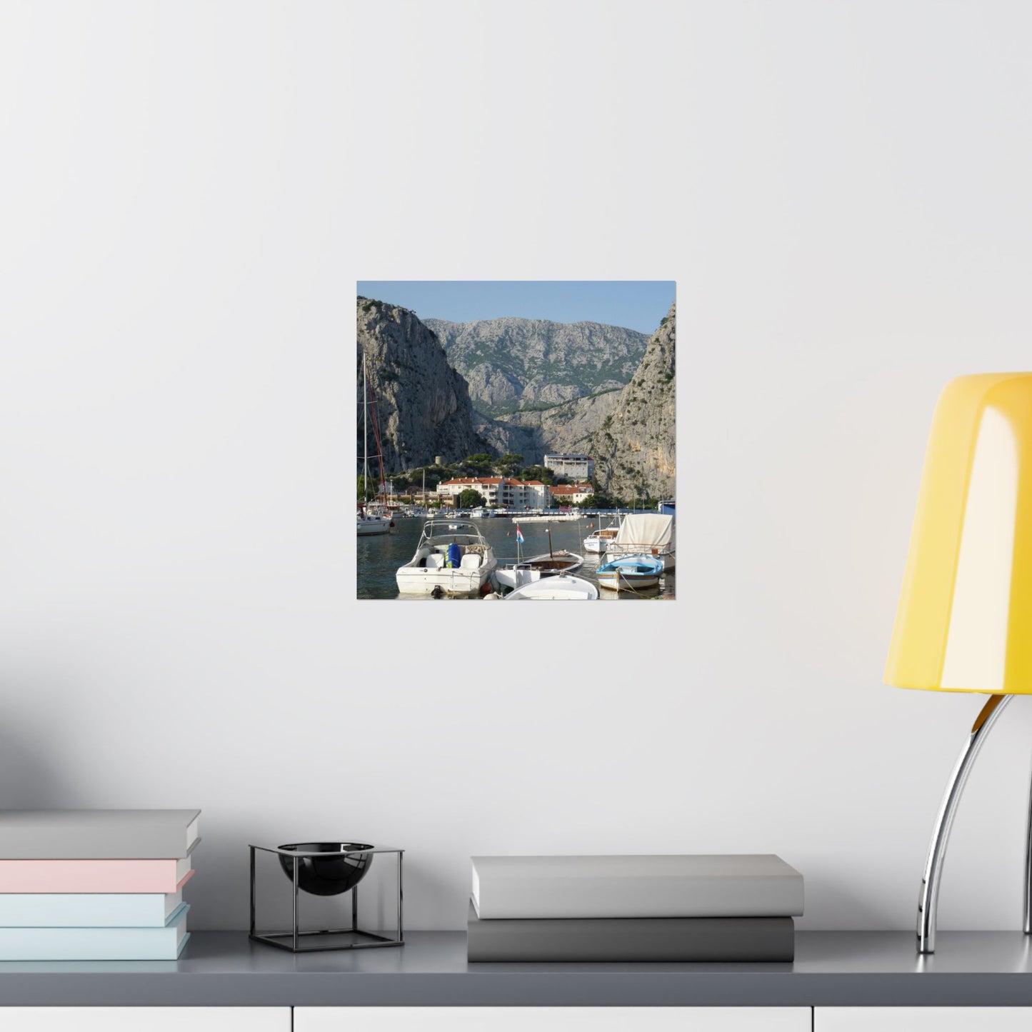 Framed photograph of a coastal scene with mountains on a white wall above a shelf.