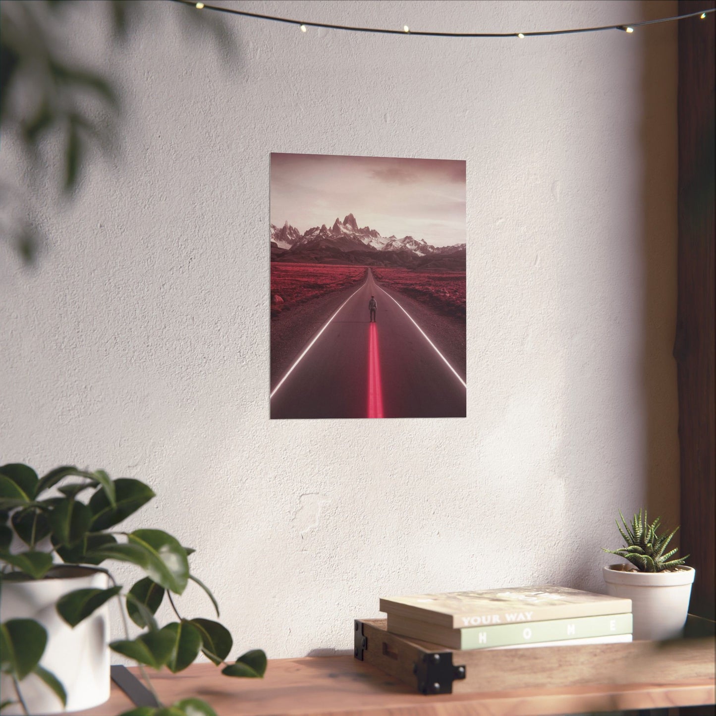 Framed artwork of a red-lit road with mountains on a white wall above a wooden desk.