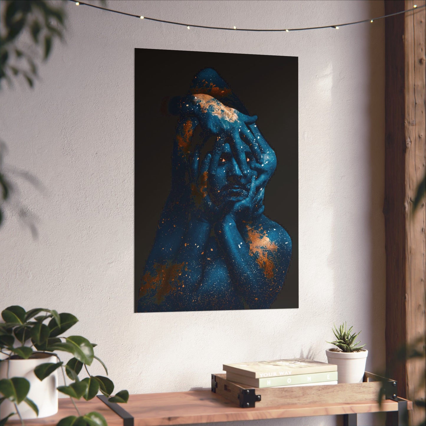 Abstract art of a person with blue and gold hues on a white wall, with a wooden table and plants below.