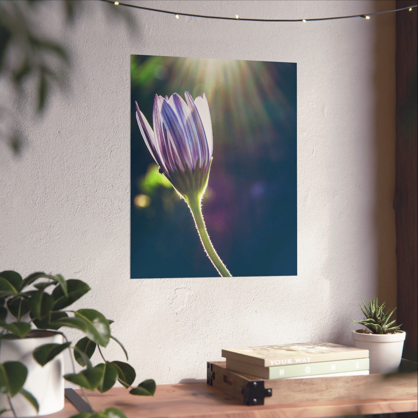 Wall tapestry with a flower design hanging on a wall above a wooden table with plants and books.