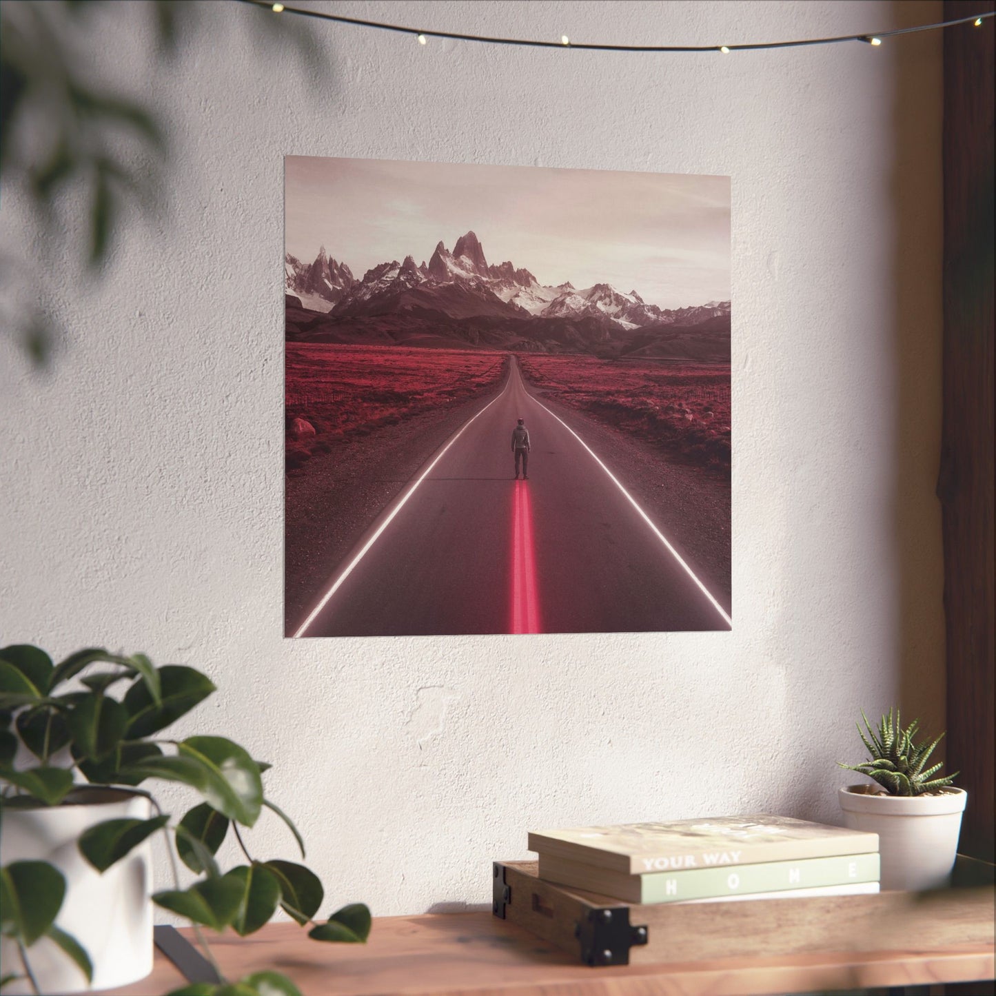 Framed artwork of a person walking on a road with mountains in the background, displayed on a wall above a desk.
