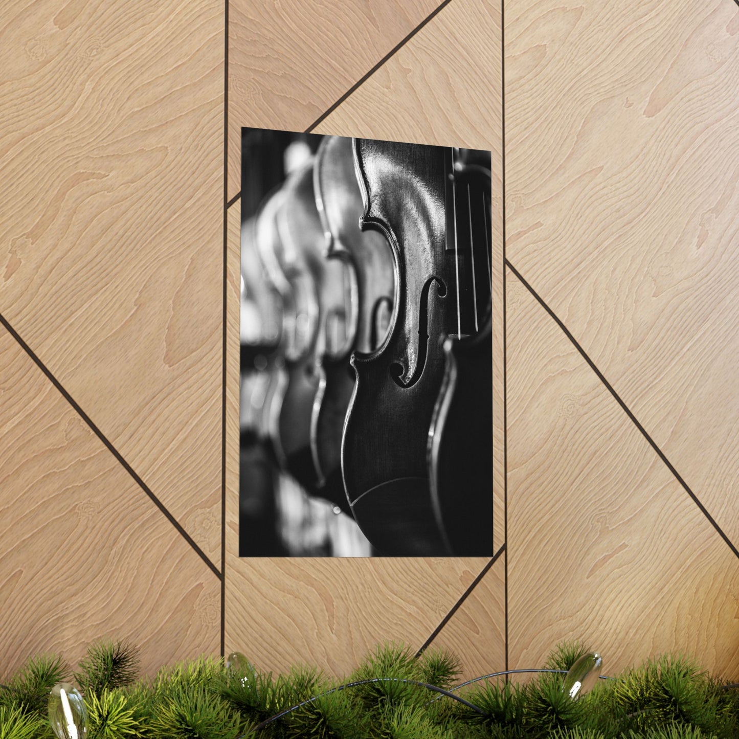 Framed black and white violin picture on a wooden wall with greenery at the bottom.
