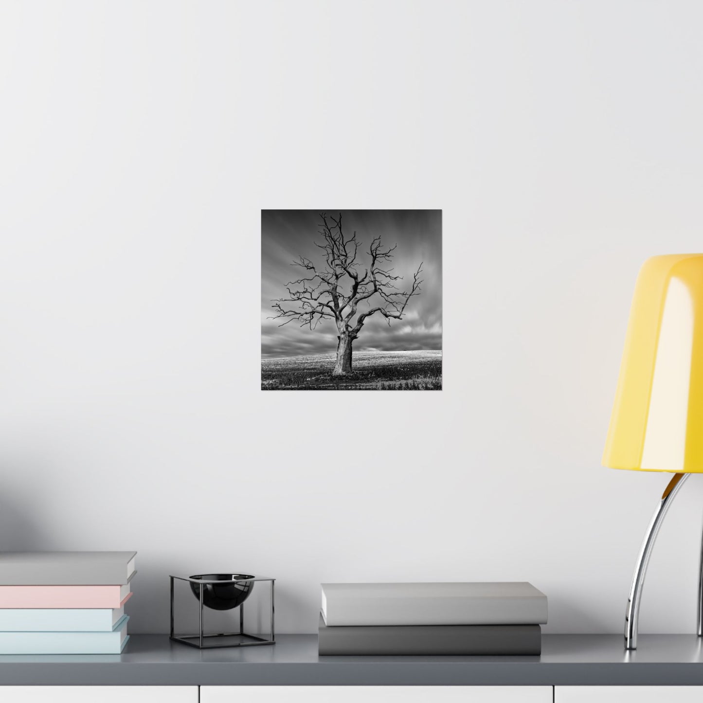 Black and white tree print on a wall above a shelf with books and decor items.