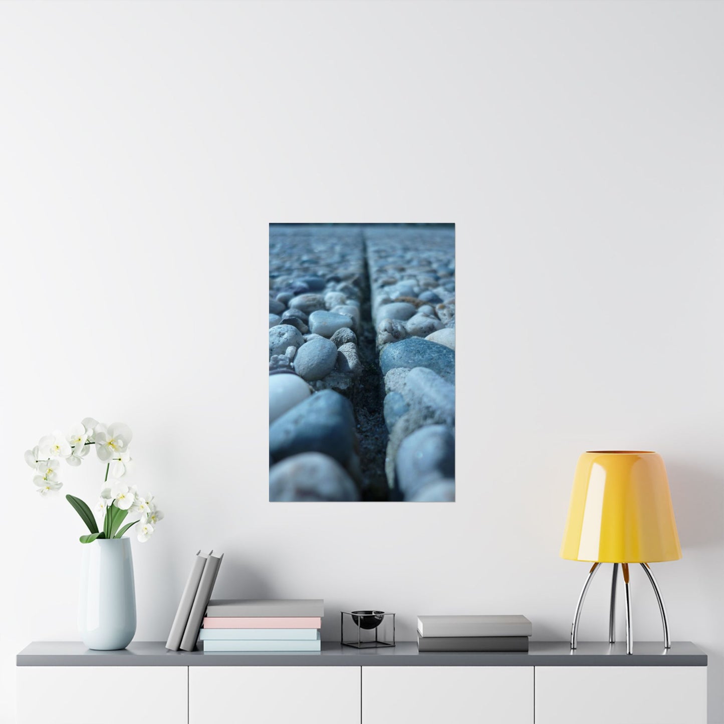 Framed artwork of pebbles on a white wall above a shelf with decor items.