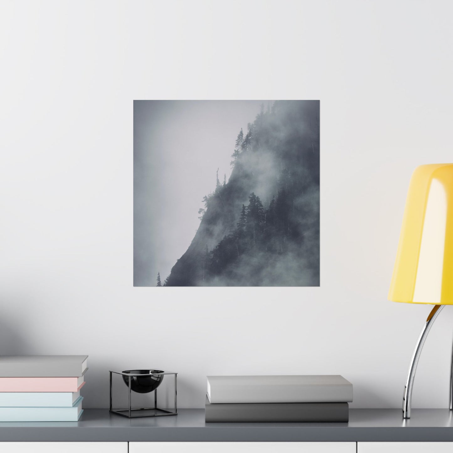 Framed artwork of a misty forest on a wall above a shelf with books and a lamp.
