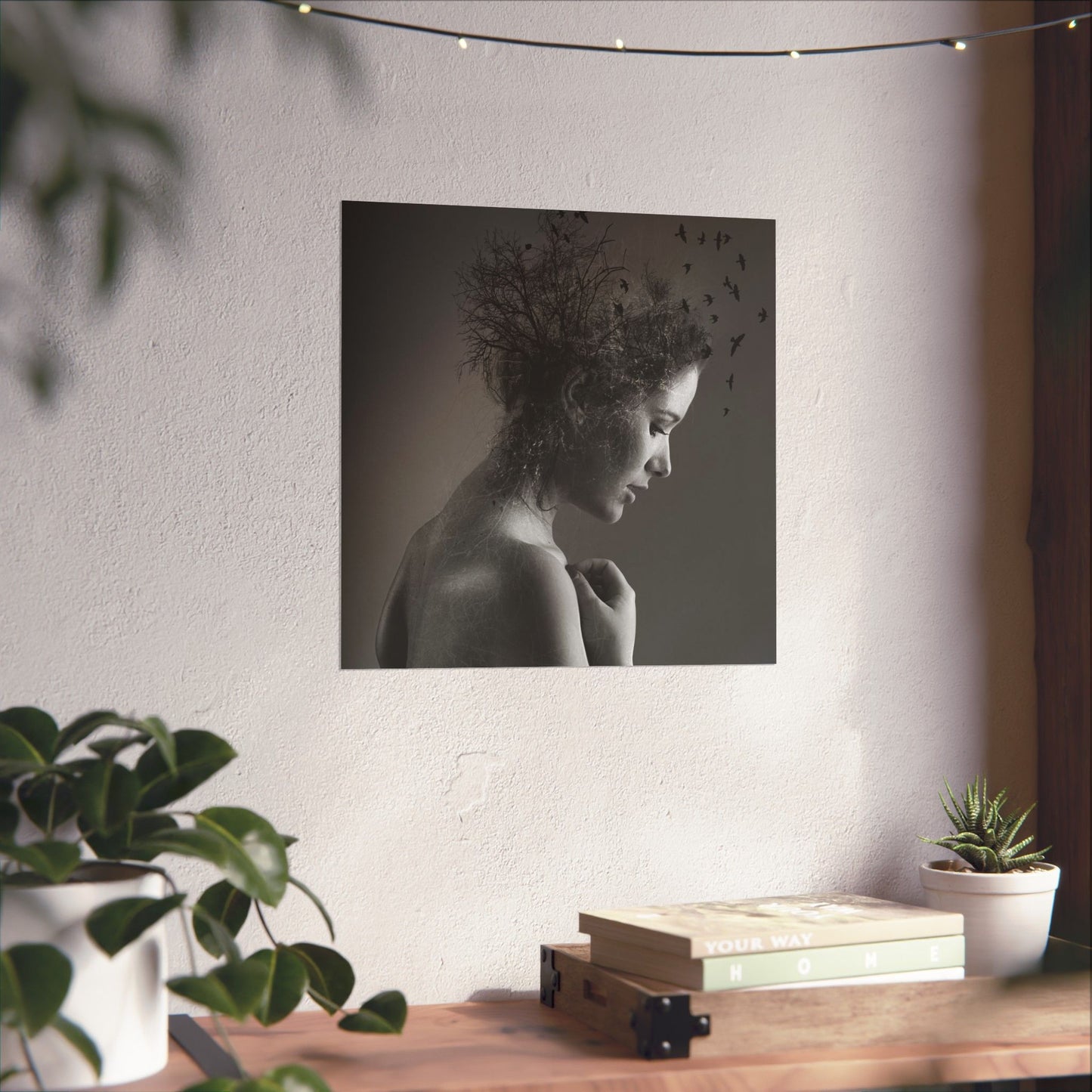 Framed black and white portrait of a woman with birds on a wall above a wooden desk with plants.
