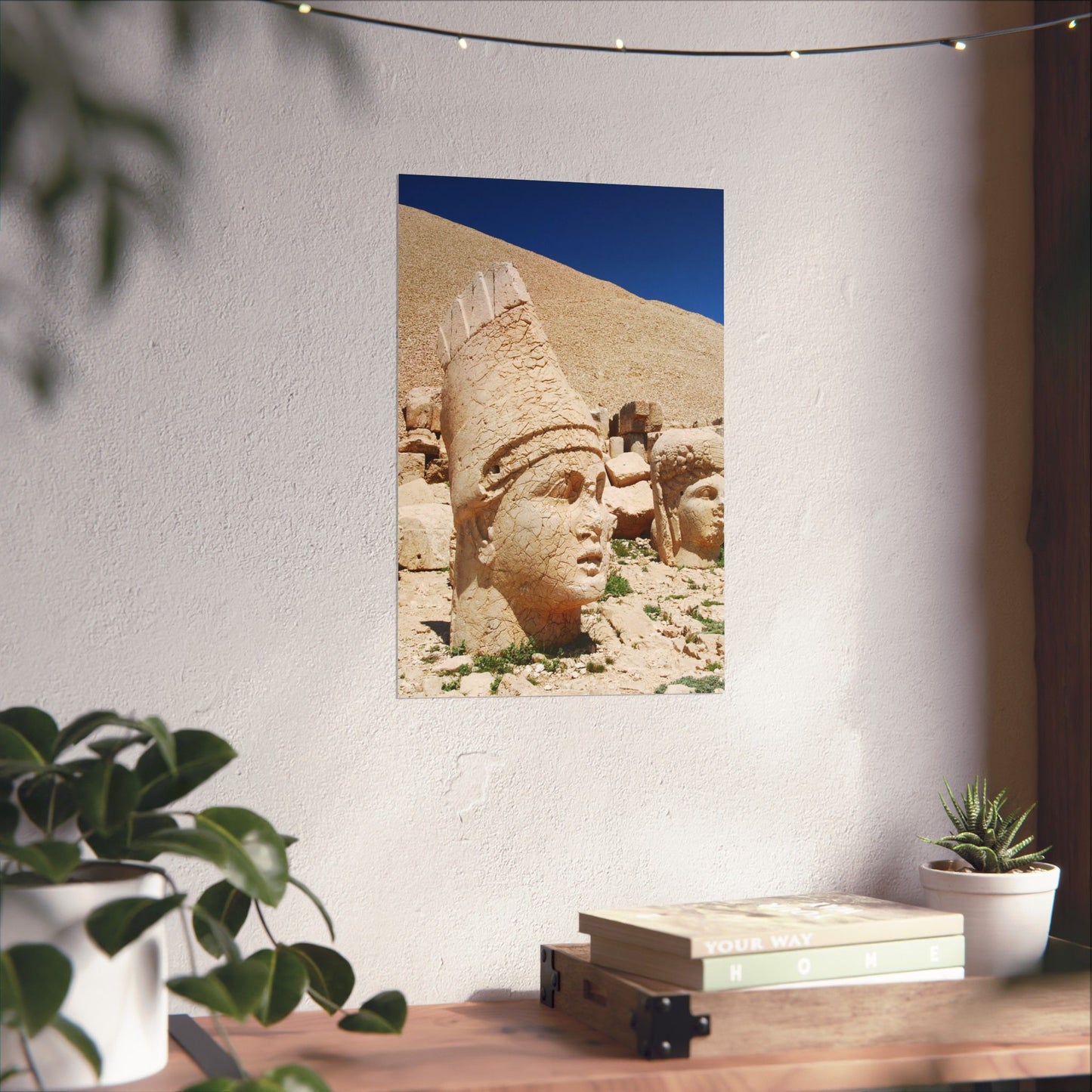 Framed photograph of ancient stone heads on a wall above a desk with plants.