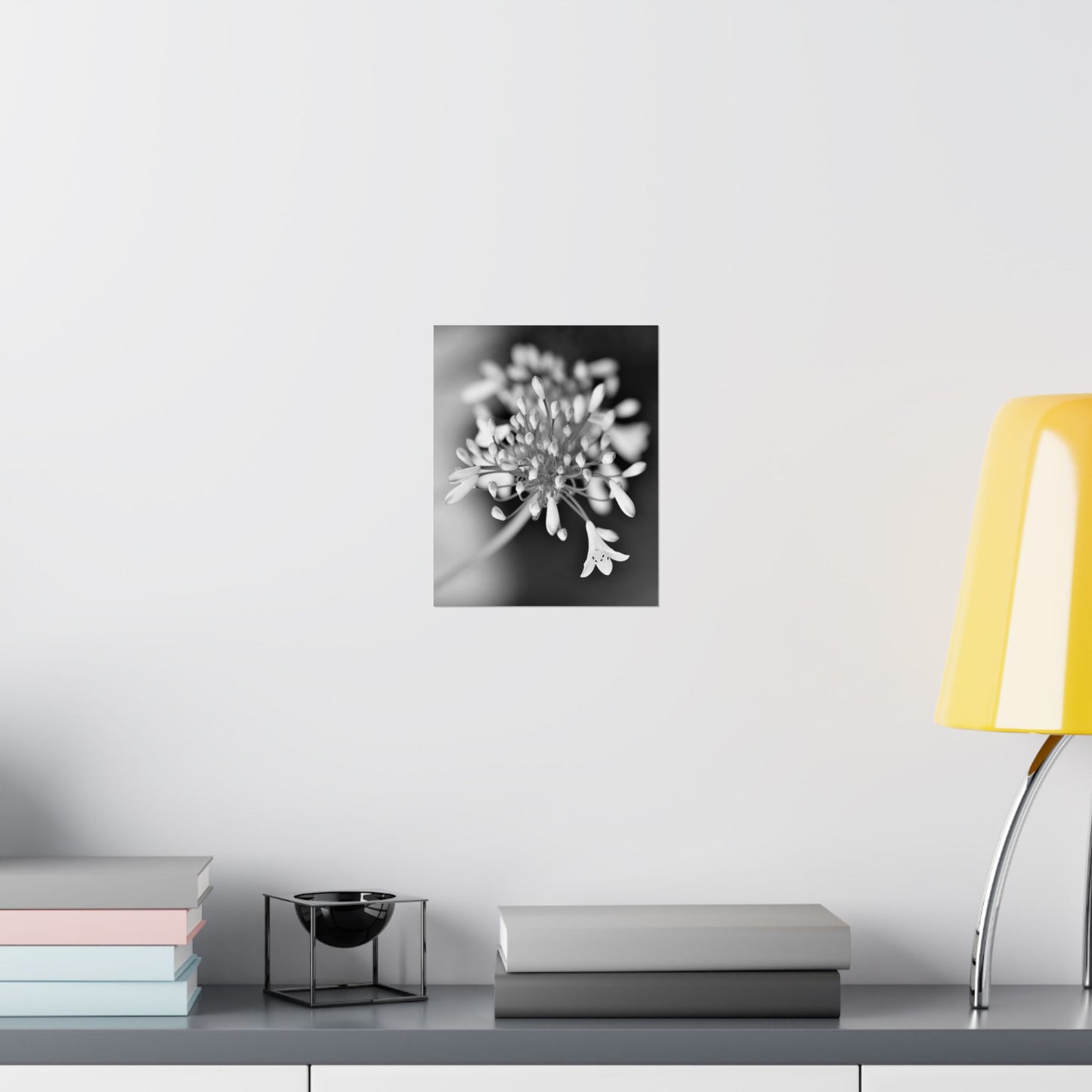 Black and white floral artwork on a wall above a desk with books and a lamp.