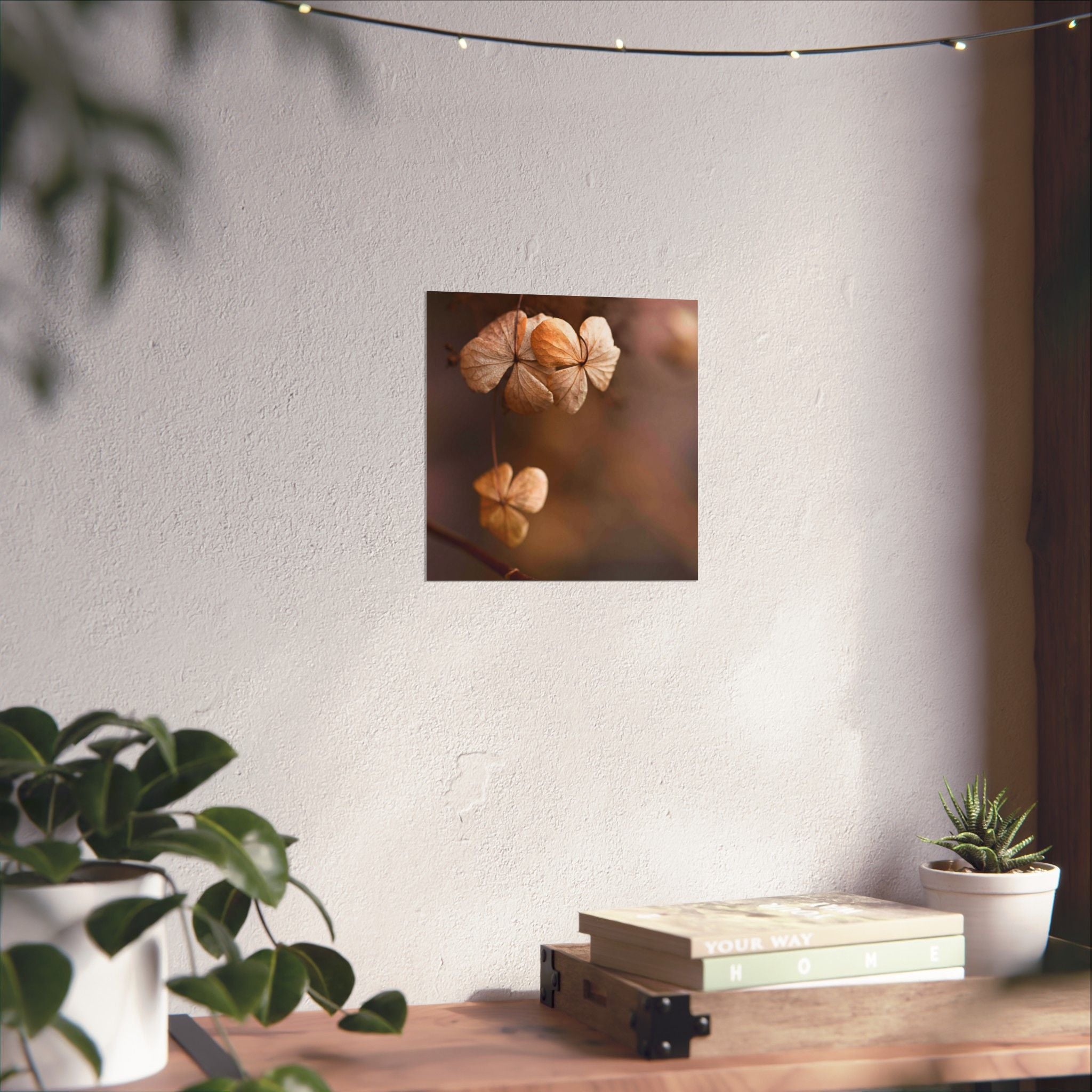 Decorative wall art of dried flowers on a white wall with plants and books on a table below.