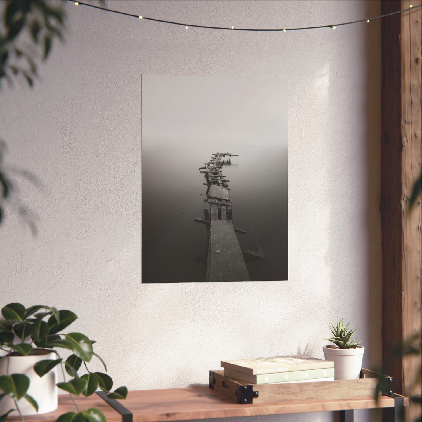 Black and white abstract art piece on a white wall with plants and books below.