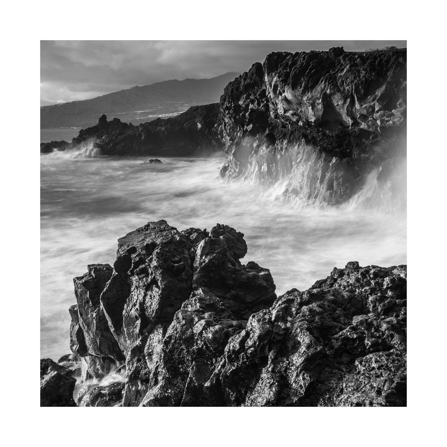 Black and white photo of waves crashing against rocky cliffs.