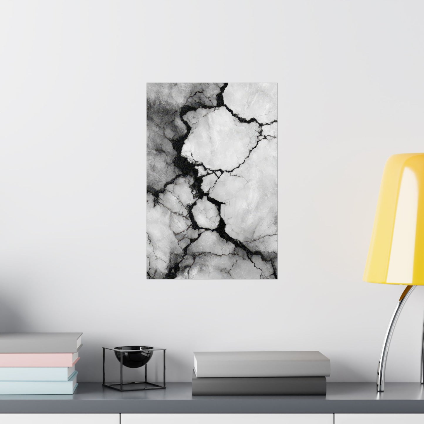 Abstract black and white marble art print on a wall above a shelf with books and a lamp.