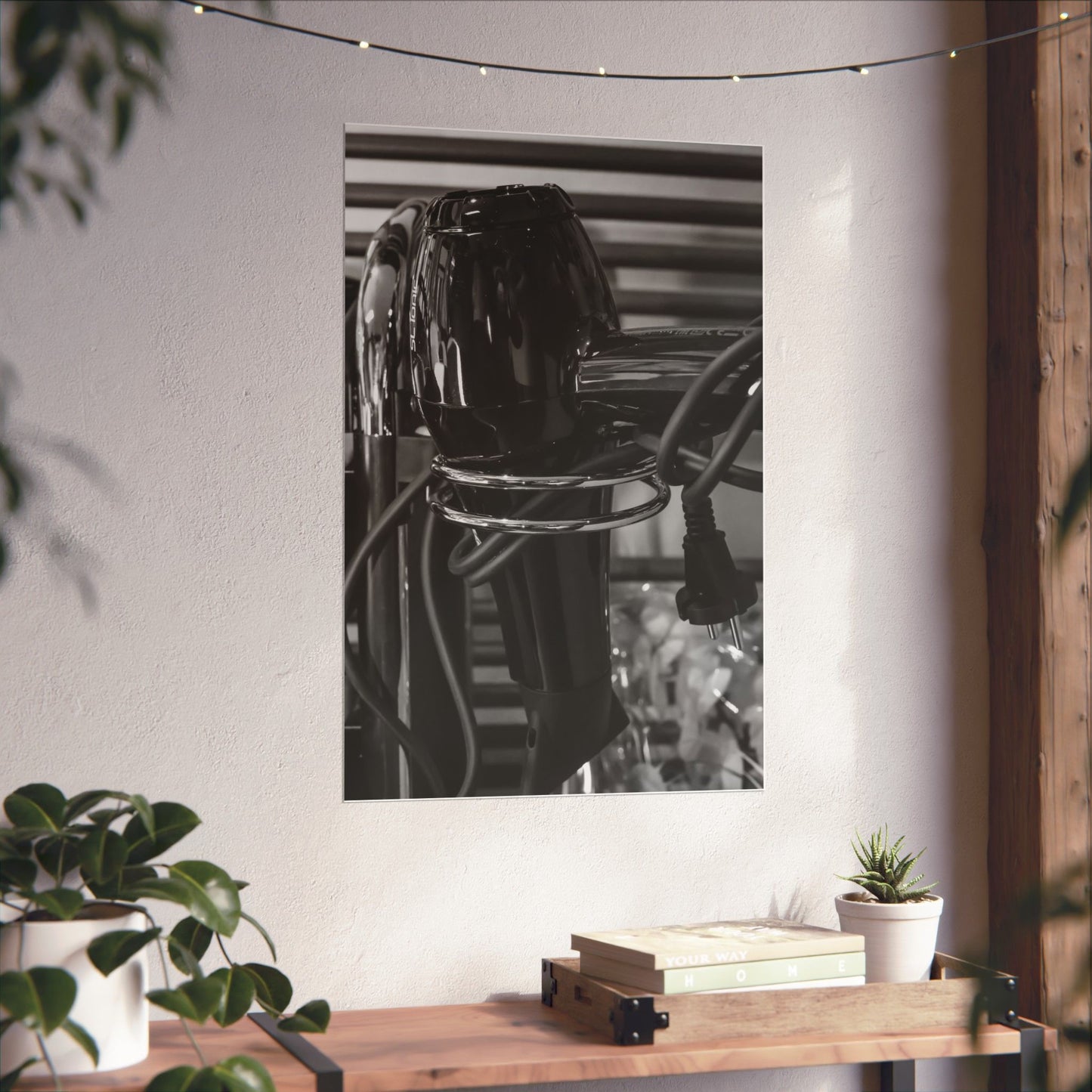 Black and white photograph of a car on a wall in a room with plants and a wooden table.